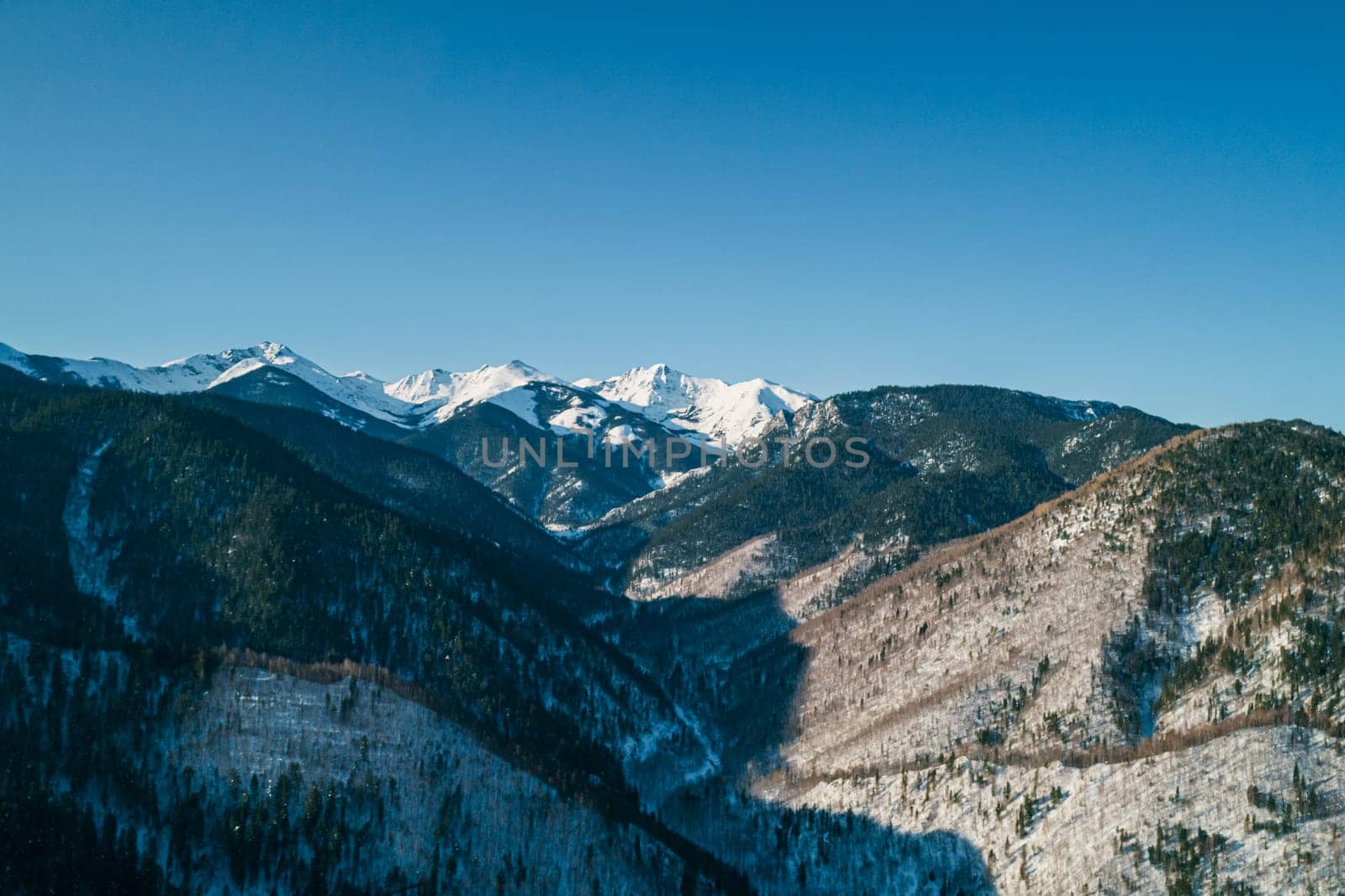 Aerial landscape mountains covered with forest and snow-capped peaks in the background. Cinematic winter mountains landscape