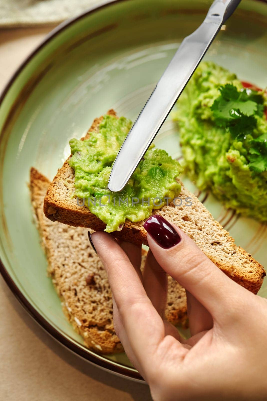 Female hands spreading vibrant piquant guacamole on slice of toasted whole grain bread. Tasty and healthy snack option