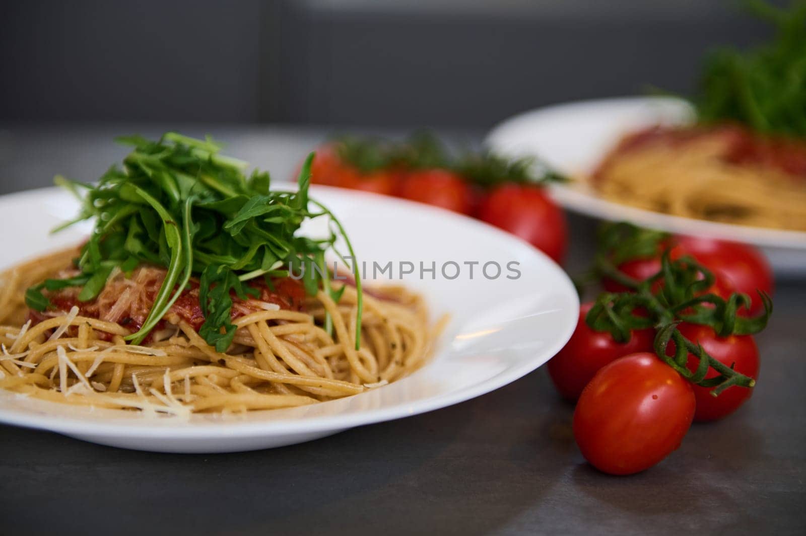 Italian spaghetti capellini with tomato sauce, parmesan cheese and arugula leaves. A branch of fresh ripe organic tomato cherry on the kitchen table.