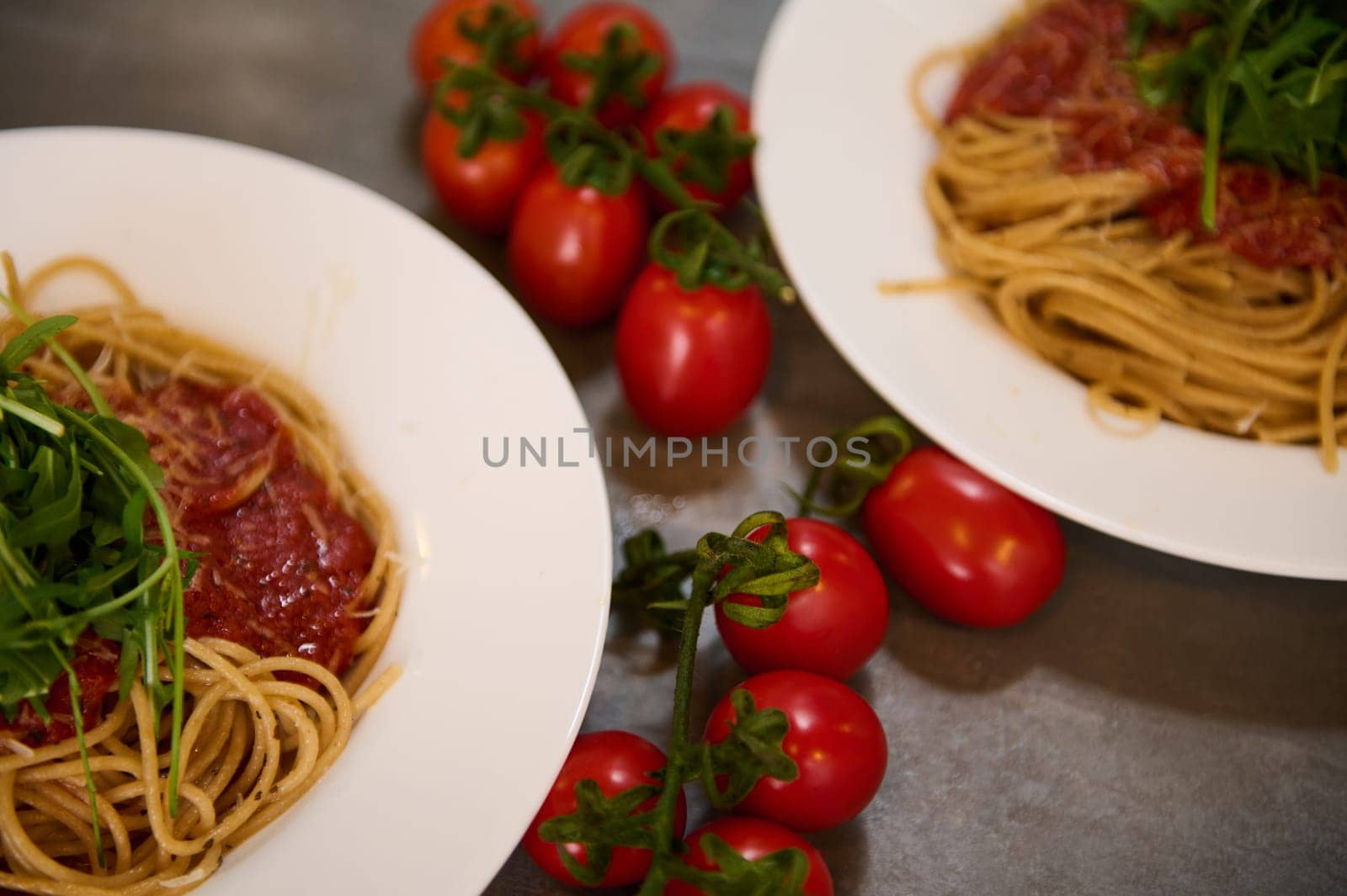 Food background. View from above of Italian spaghetti garnished with arugula leaves. Italian cuisine, culture and traditions. A bunch of red juicy ripe cherry tomatoes on the kitchen table