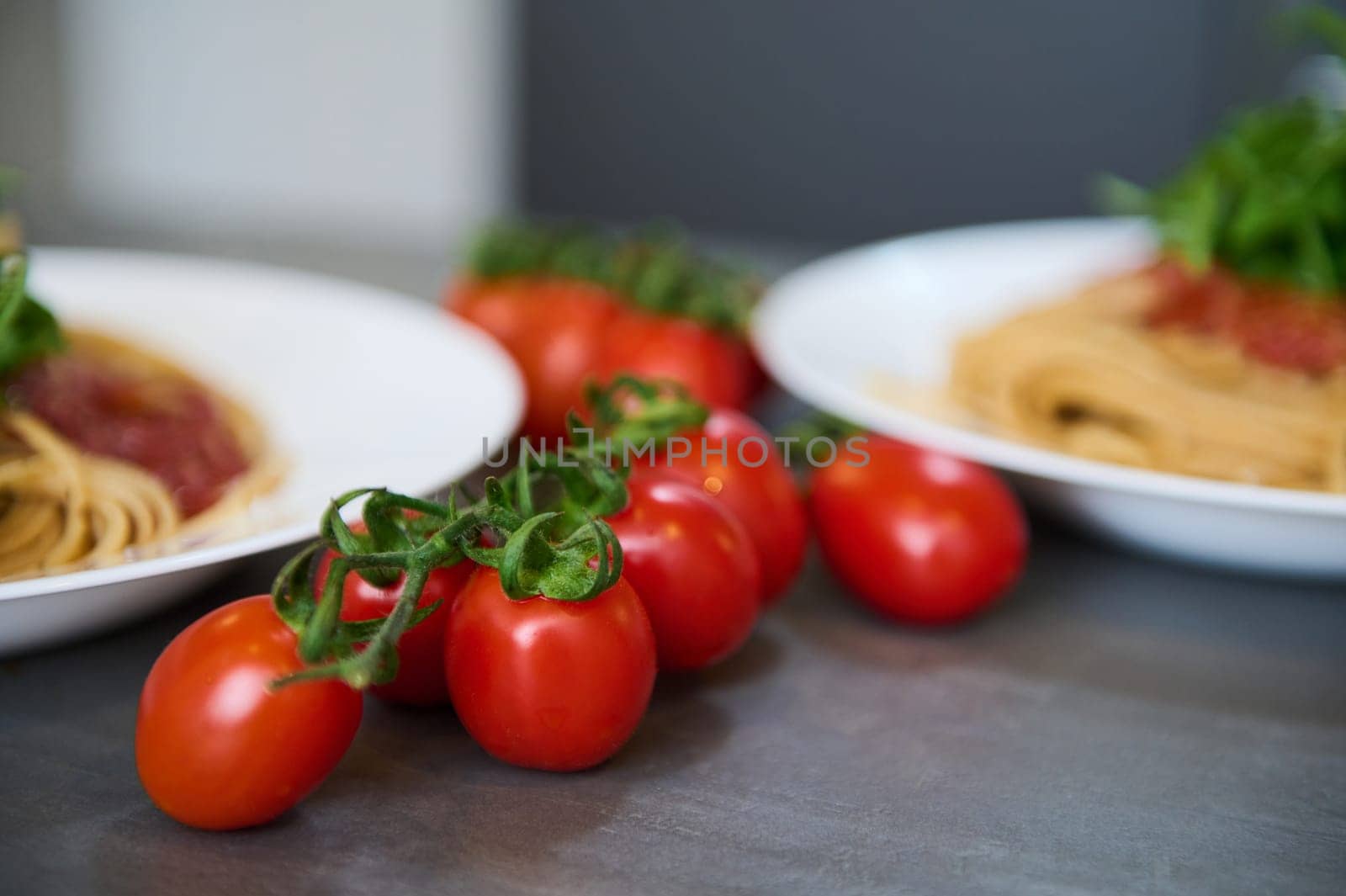 Selective focus on a bunch of red ripe organic tomatoes on the kitchen table, near two plates with Italian pasta. Food background. Still life