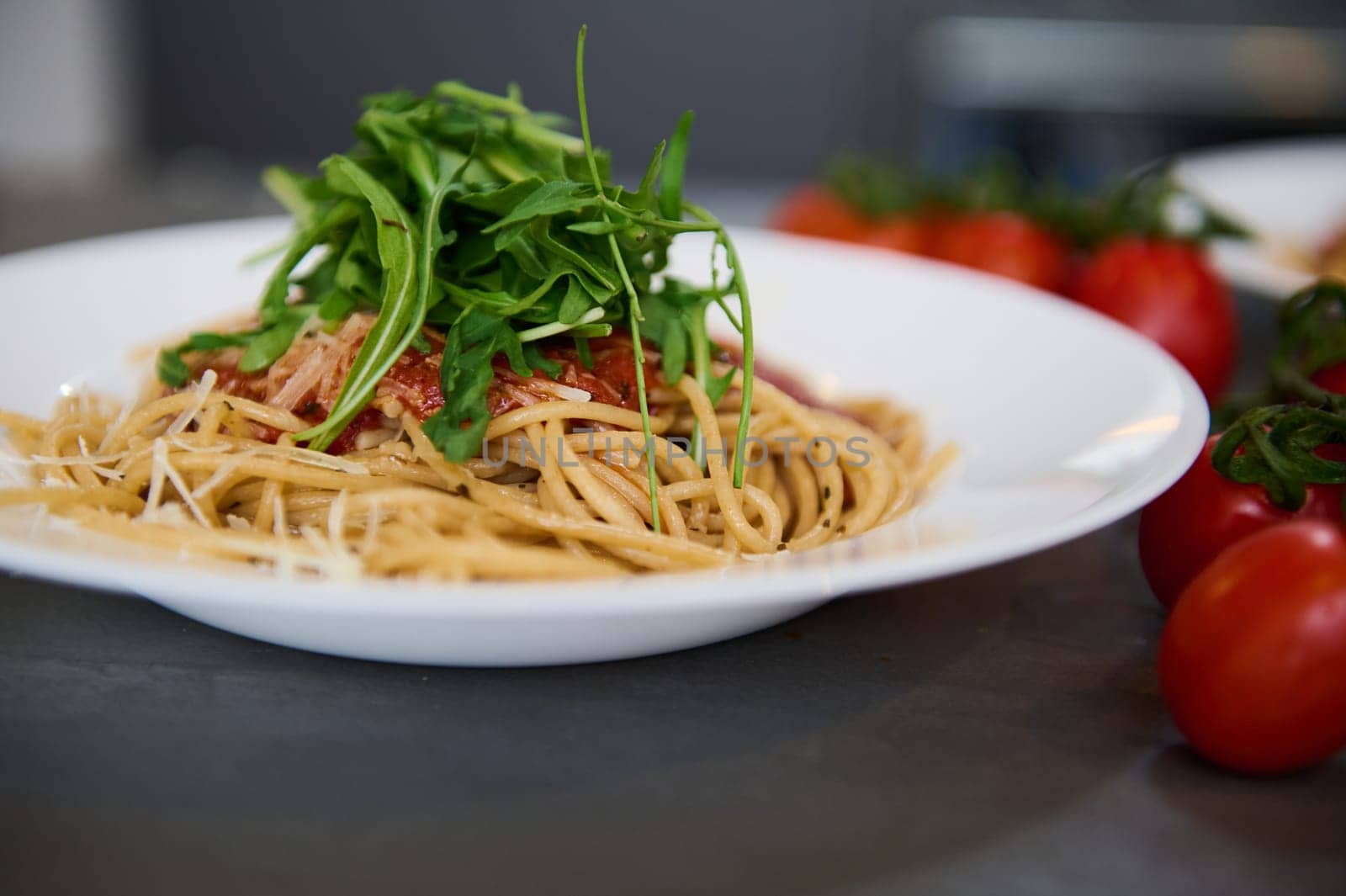 Italian pasta. Fresh homemade spaghetti capellini pasta with tomato sauce and garnished with arugula green leaves on the kitchen table near a branch of organic tomato cherry. Food background