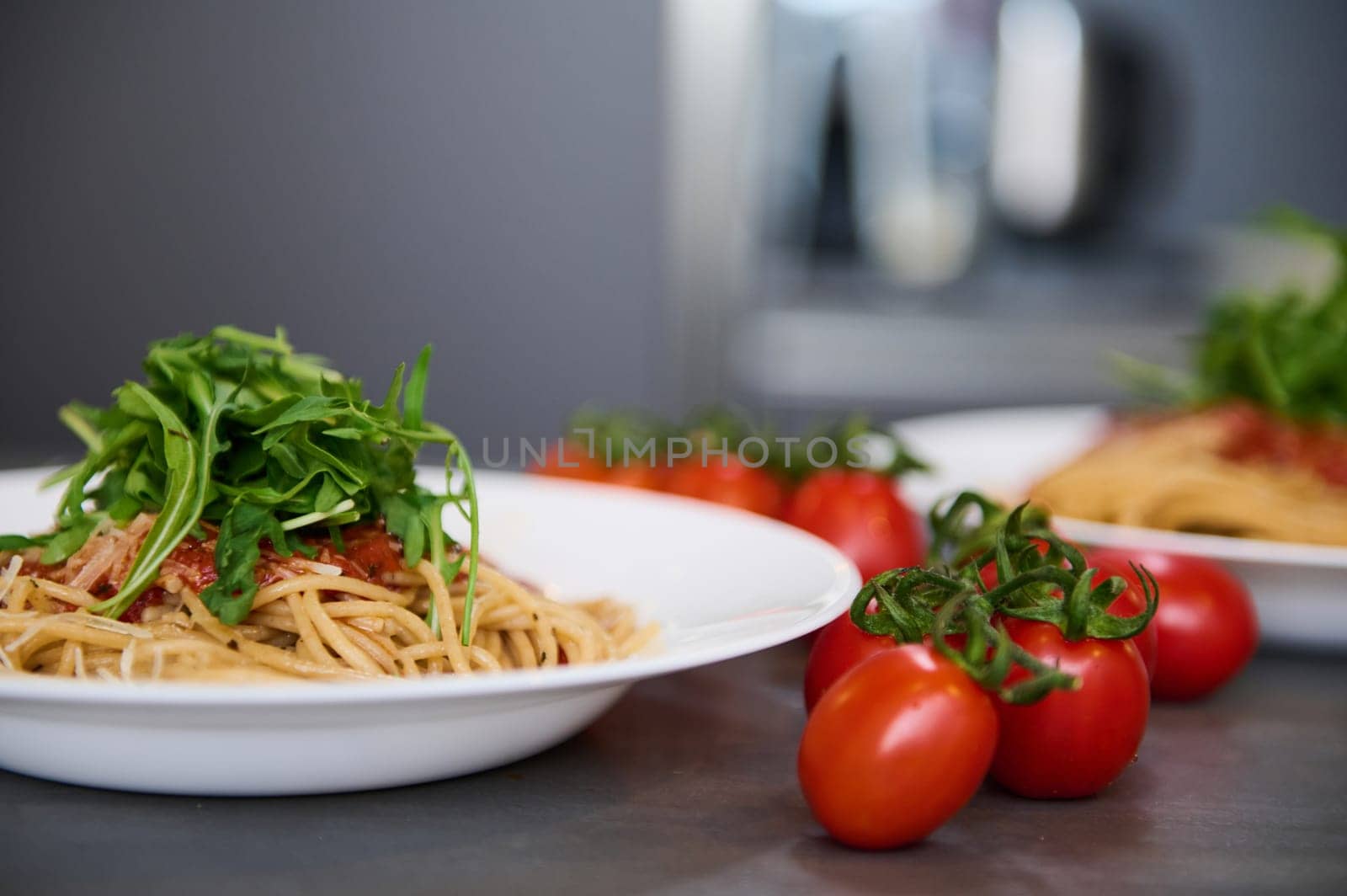 A served dish with delicious Italian pasta with tomato sauce, seasoned with fresh arugula leaves and grated parmesan cheese on pasta in white plate. Decoration of dish. Italian cuisine. Food backdrop