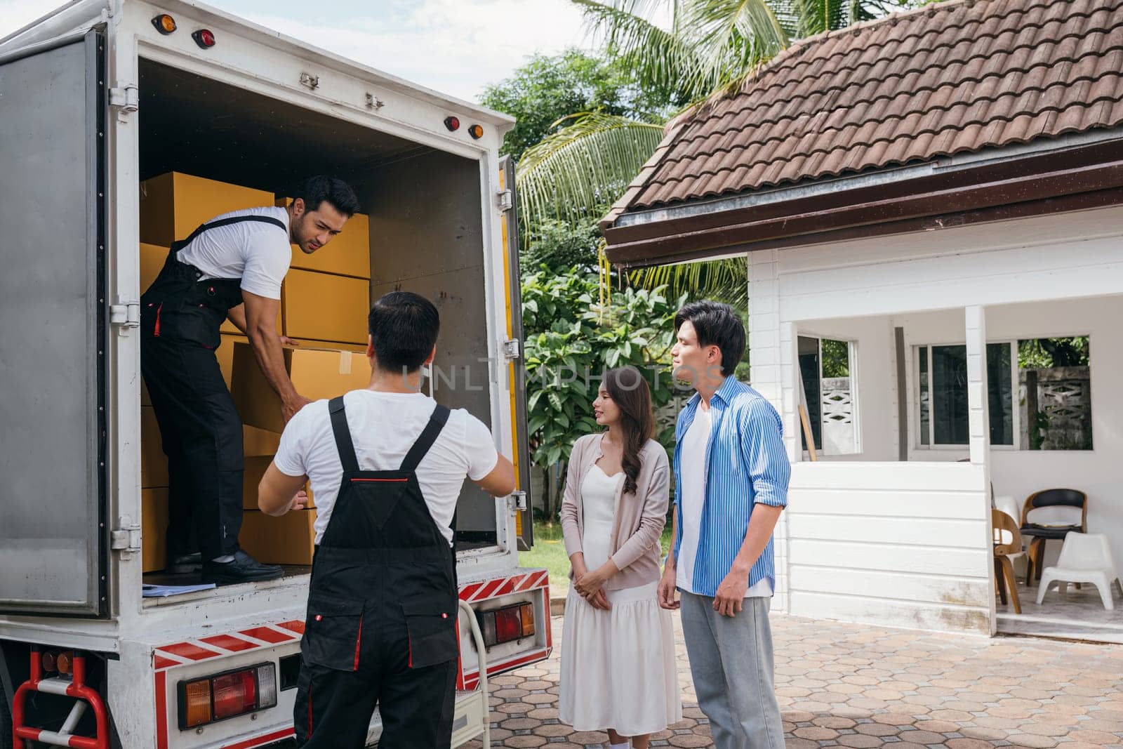 A couple receives professional assistance in moving to their new house. The teamwork of employees is evident as they unload and lift cardboard boxes during the relocation. Moving Day Concept by Sorapop