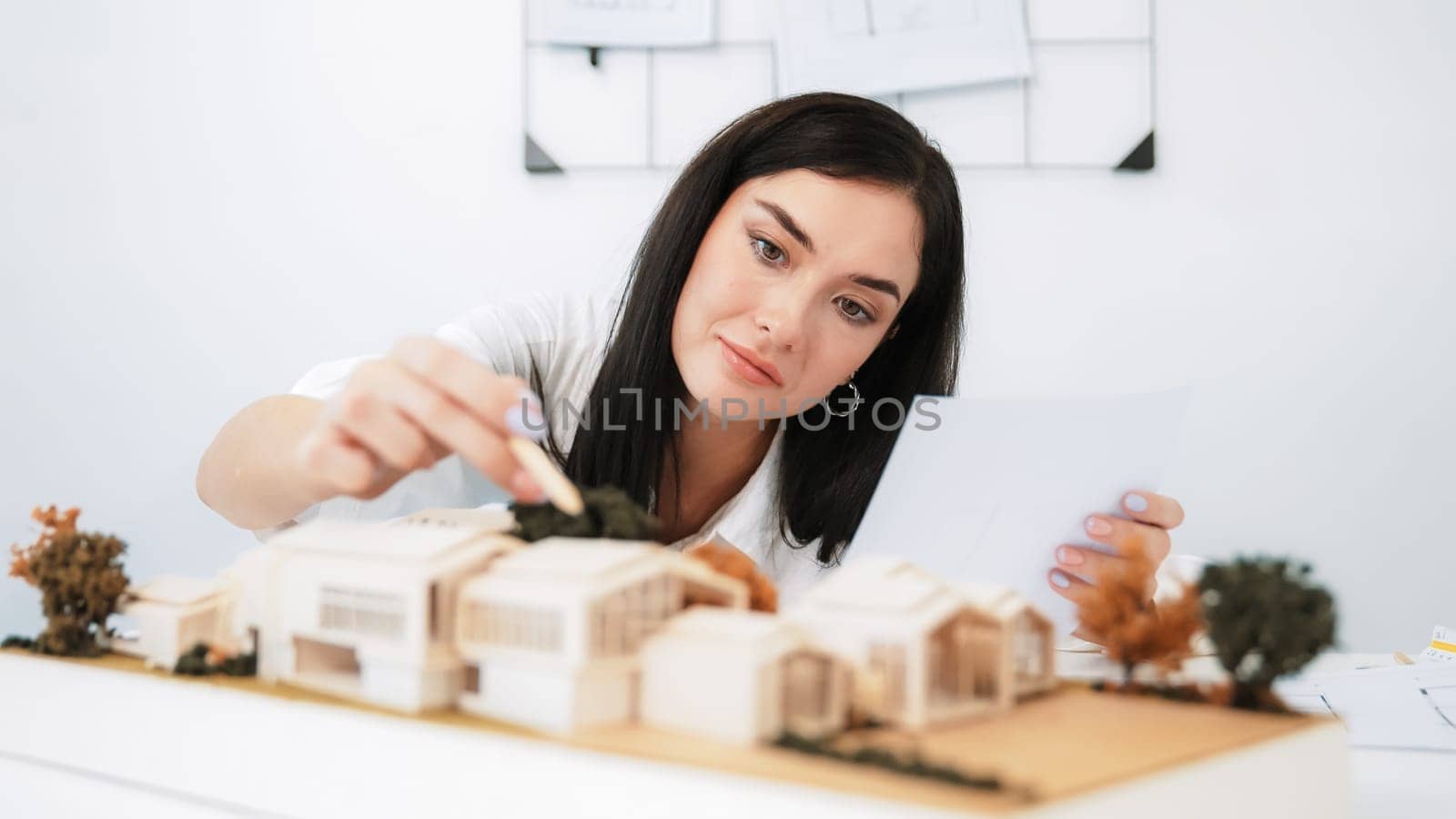 Closeup portrait image of young beautiful architect focus on measures the architectural model with blueprint placed on table in modern meeting room. Creative business design concept. Immaculate.