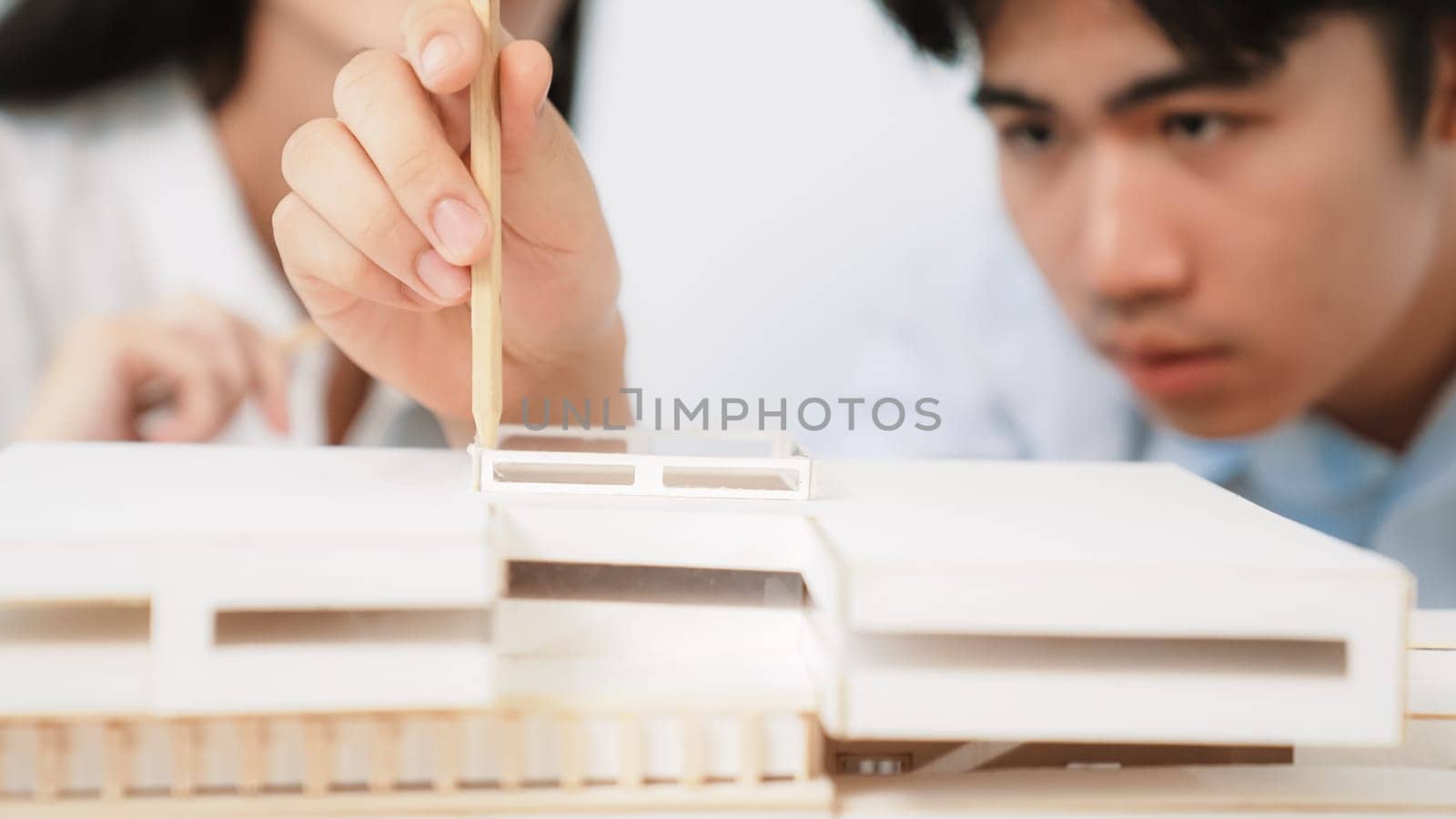 Closeup of young professional architect team work together to use pencil testing house model durability about house construction. Creative design and teamwork concept. Focus on hand. Immaculate.