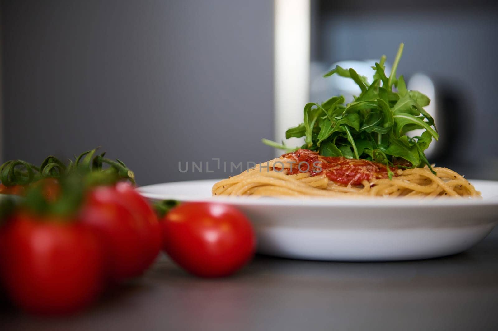 Italian pasta capellini with tomato sauce and basil green arugula leaves on white plates near a bunch of red cherry tomato on blurred foreground. Italian cuisine, culture and traditions. Epicure.
