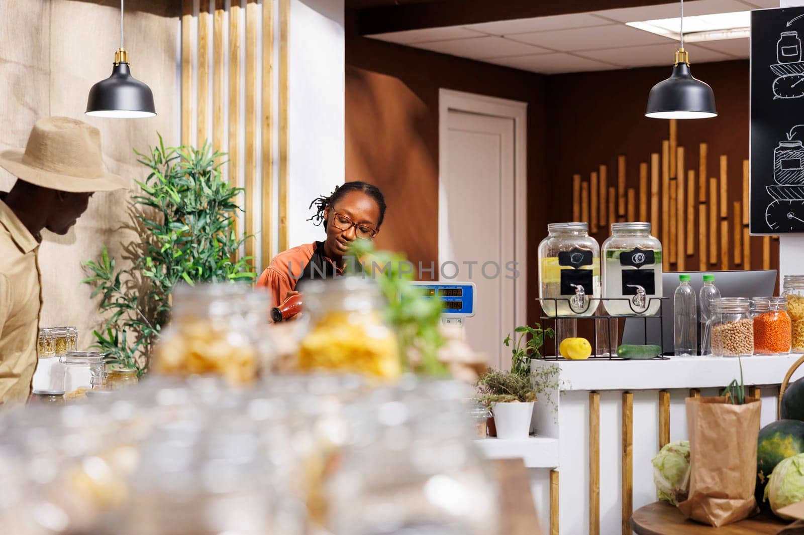 At the checkout desk, a young black woman is taking goods out of the basket for weighing. African American female cashier being of service to the male customer at the counter.