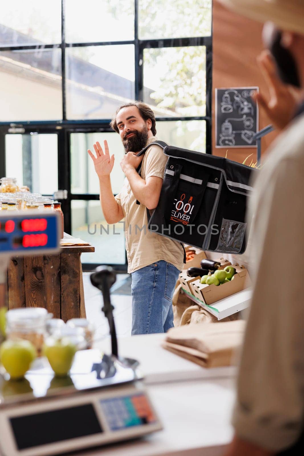 Caucasian male courier leaving eco friendly convenience store to deliver locally grown produce to customers. Young delivery man carrying thermal bag with takeaway from sustainable supermarket.