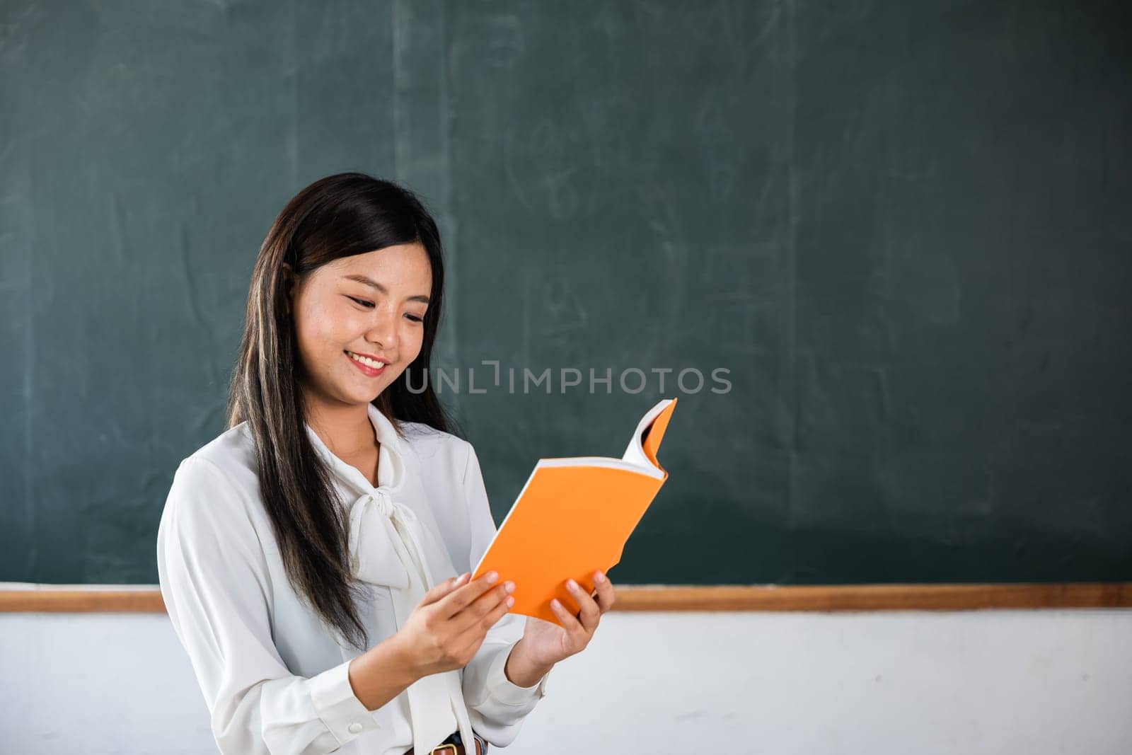 A woman is reading a book in a classroom. She is smiling and she is enjoying the book