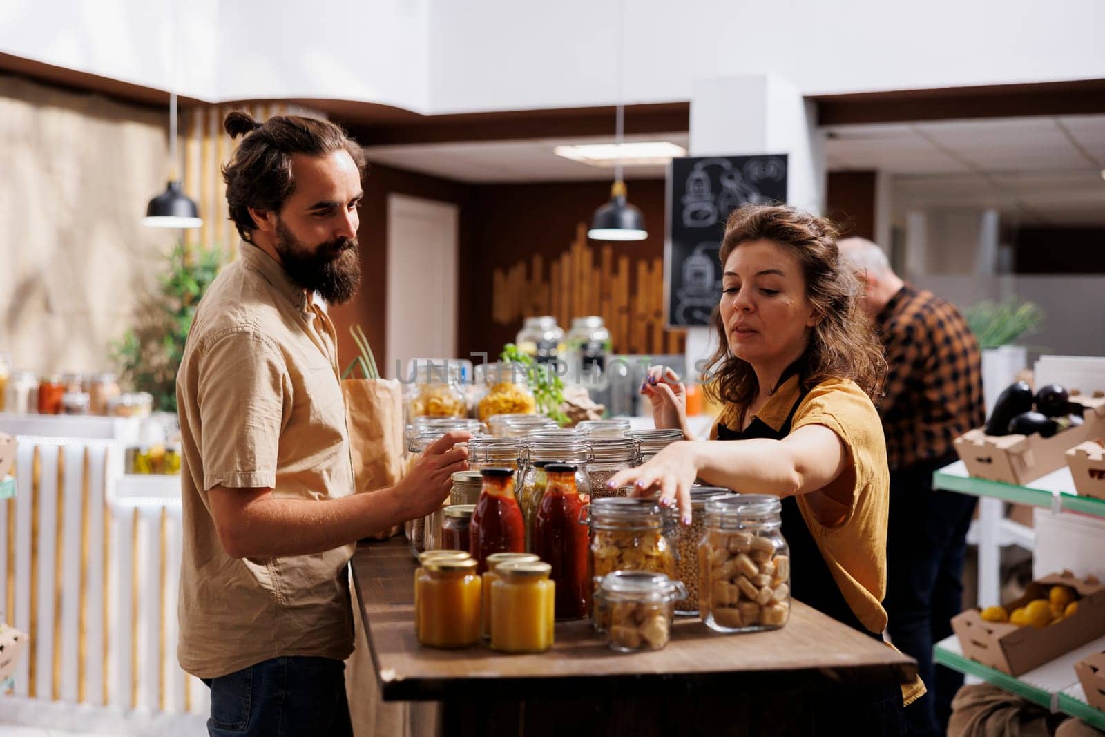 Farmer showcasing her products in zero waste marketplace location, selling bio food to interested buyer. Local trader selling her organic bulk products merchandise during event