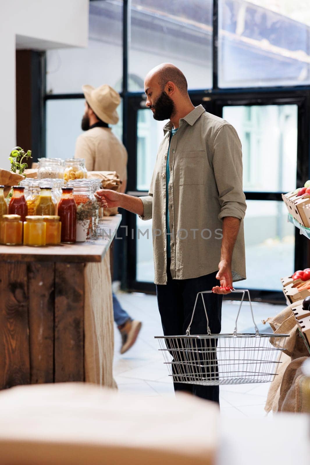 Arab man walks through the aisles of eco friendly market, intent on purchasing sustainable food. Male client with basket shopping for fresh, organic products at local small business.