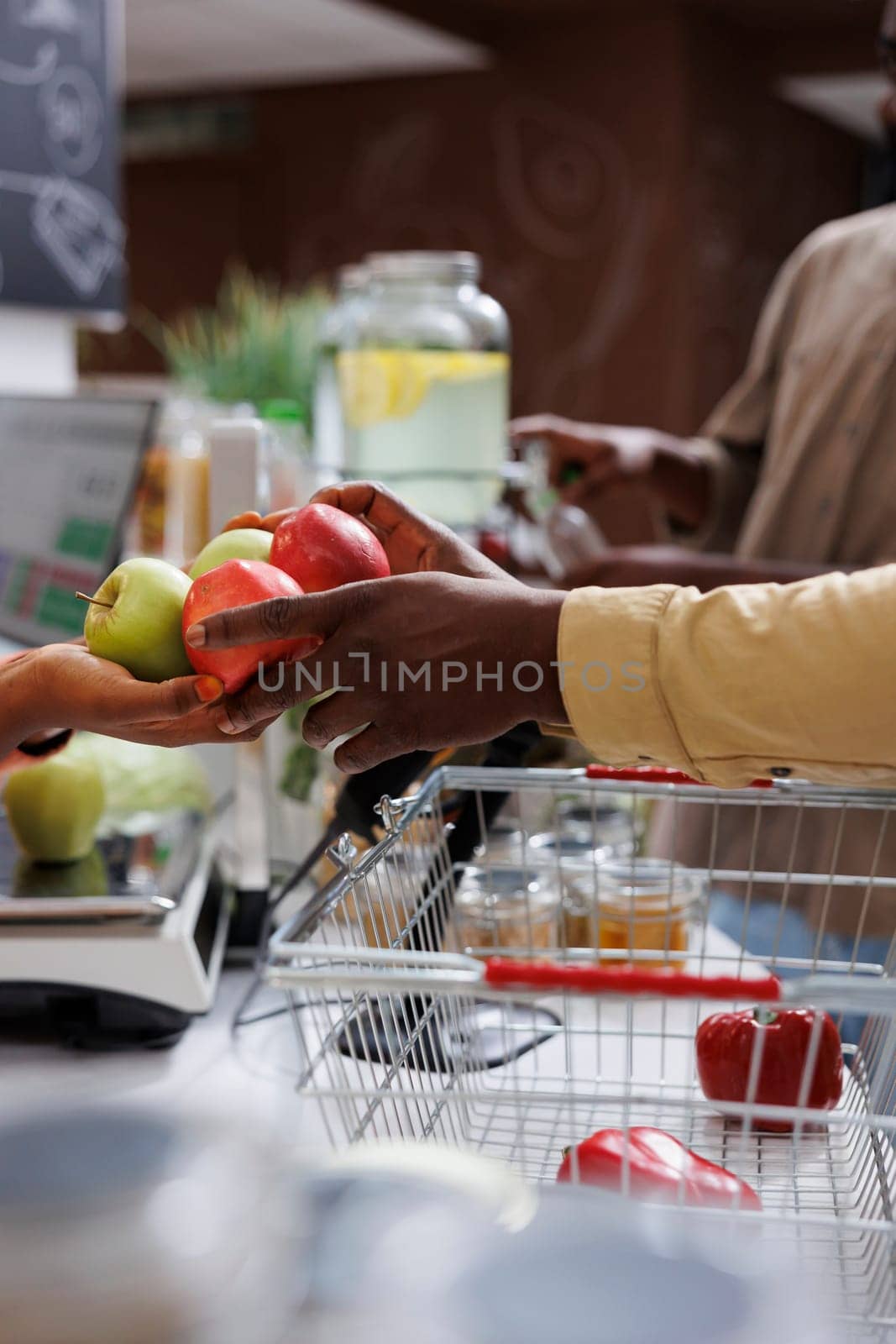 The close-up shows two African Americans' hands carrying a bunch of apples above the checkout counter. The image focused on a male customer giving fruits to the black vendor for weighing.