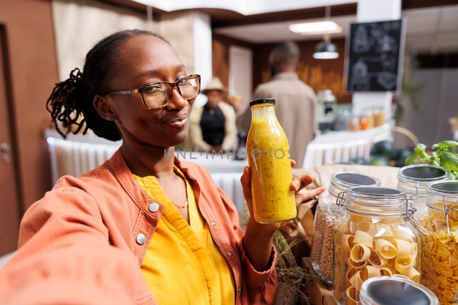 A young black woman films herself in a zero-waste shop promoting eco friendly grocery shopping. She highlights fresh, homegrown products and engages her online audience through vlogging.