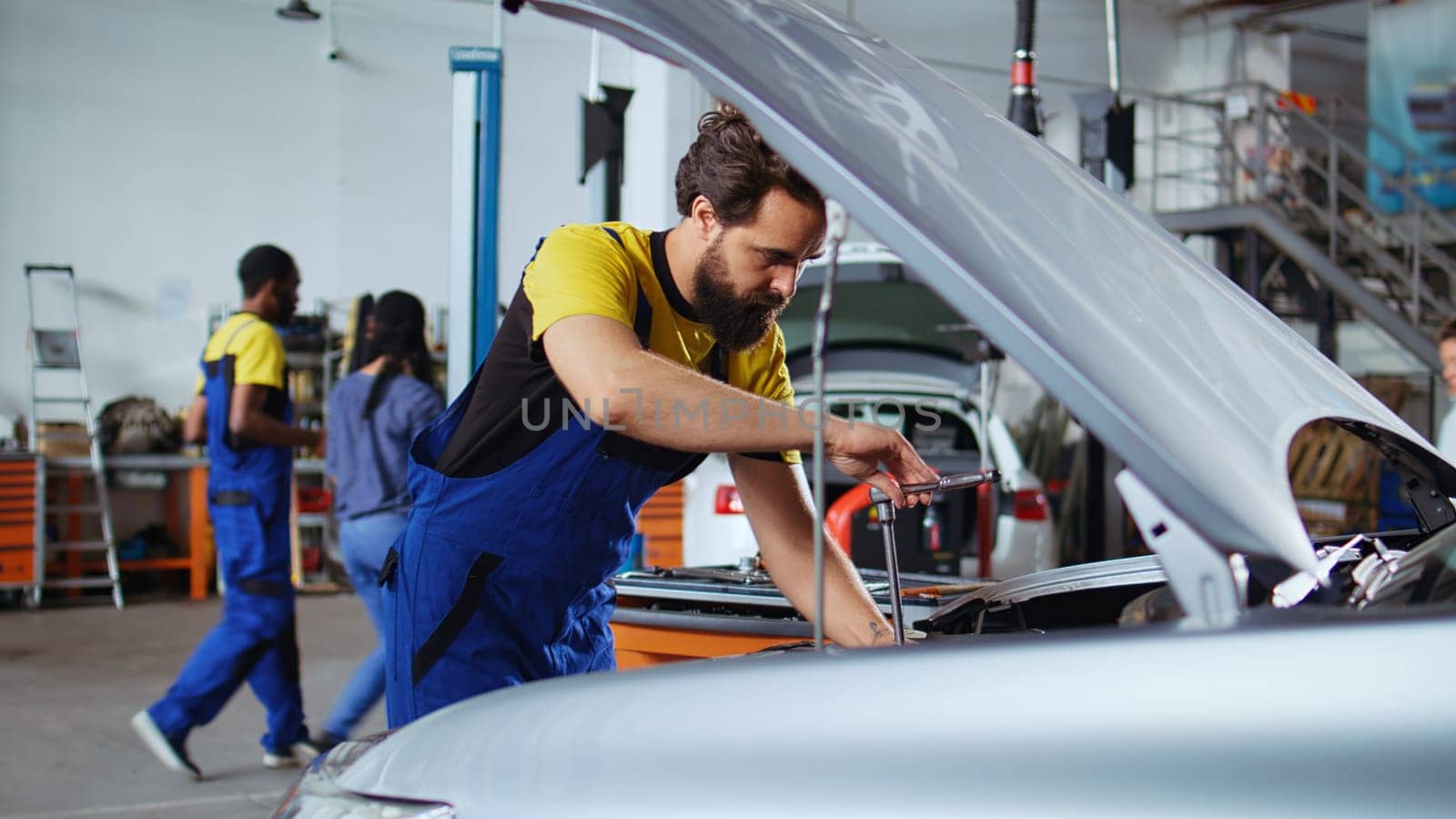 Licensed repairman in car service picks torque wrench from work station bench, using it to tighten bolts after replacing engine. Garage worker uses professional tools to fix client automobile