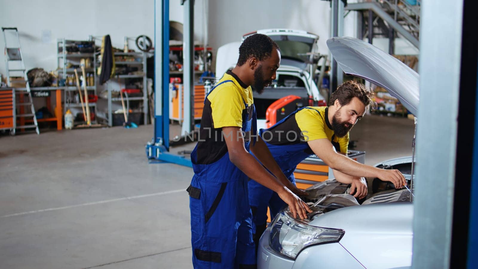 Trained technicians in auto repair shop working together on fixing car, discussing best options. Professional and colleague collaborating on servicing broken vehicle, checking for defective components