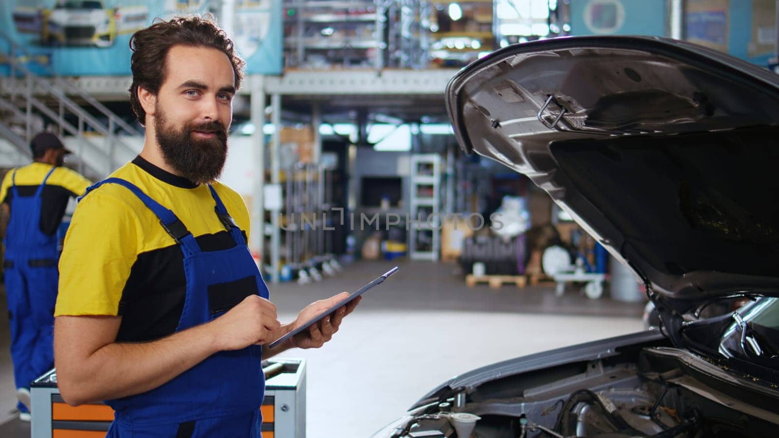 Dolly in shot of serviceman assisting customer with car maintenance in repair shop. Employee in garage workspace looking over automobile parts with woman, repairing her vehicle during routine checkup