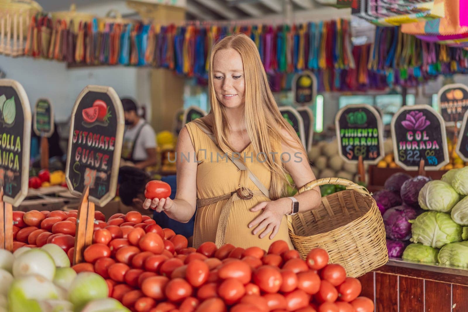 In a grocery store, a pregnant woman stands by a fruit stand, surrounded by various natural foods. She is in a public space where the local market offers whole foods for trade Pregnant woman buying organic vegetables and fruits at Mexican style farmers market