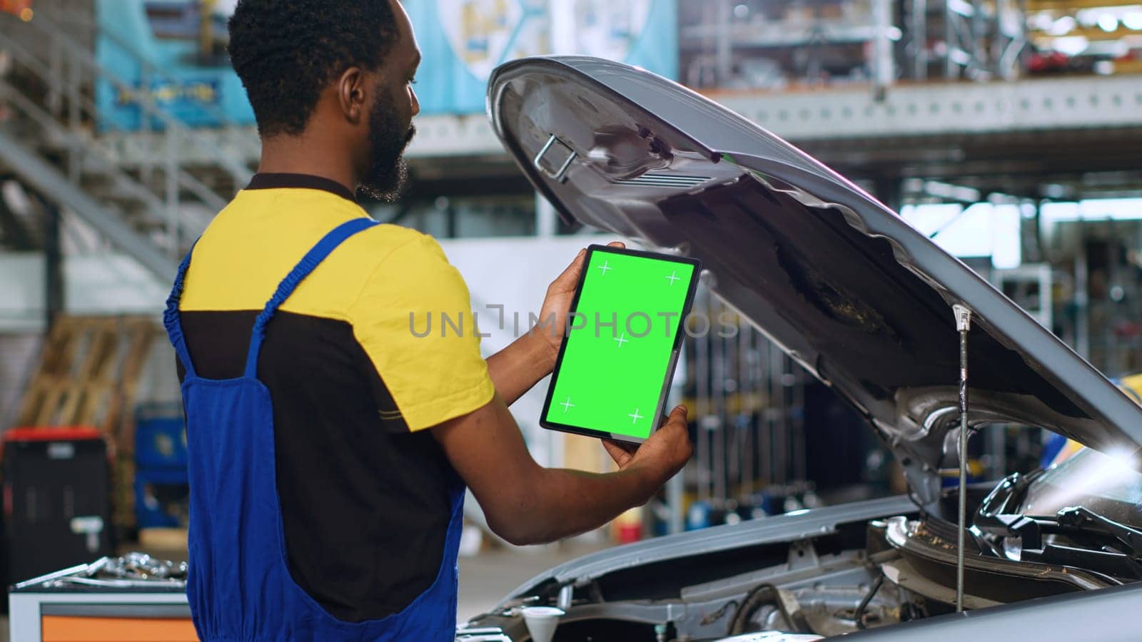 Trained repairman using green screen tablet in car service to order new parts for busted vehicle. Repair shop employee using chroma key device to look online for replacing components