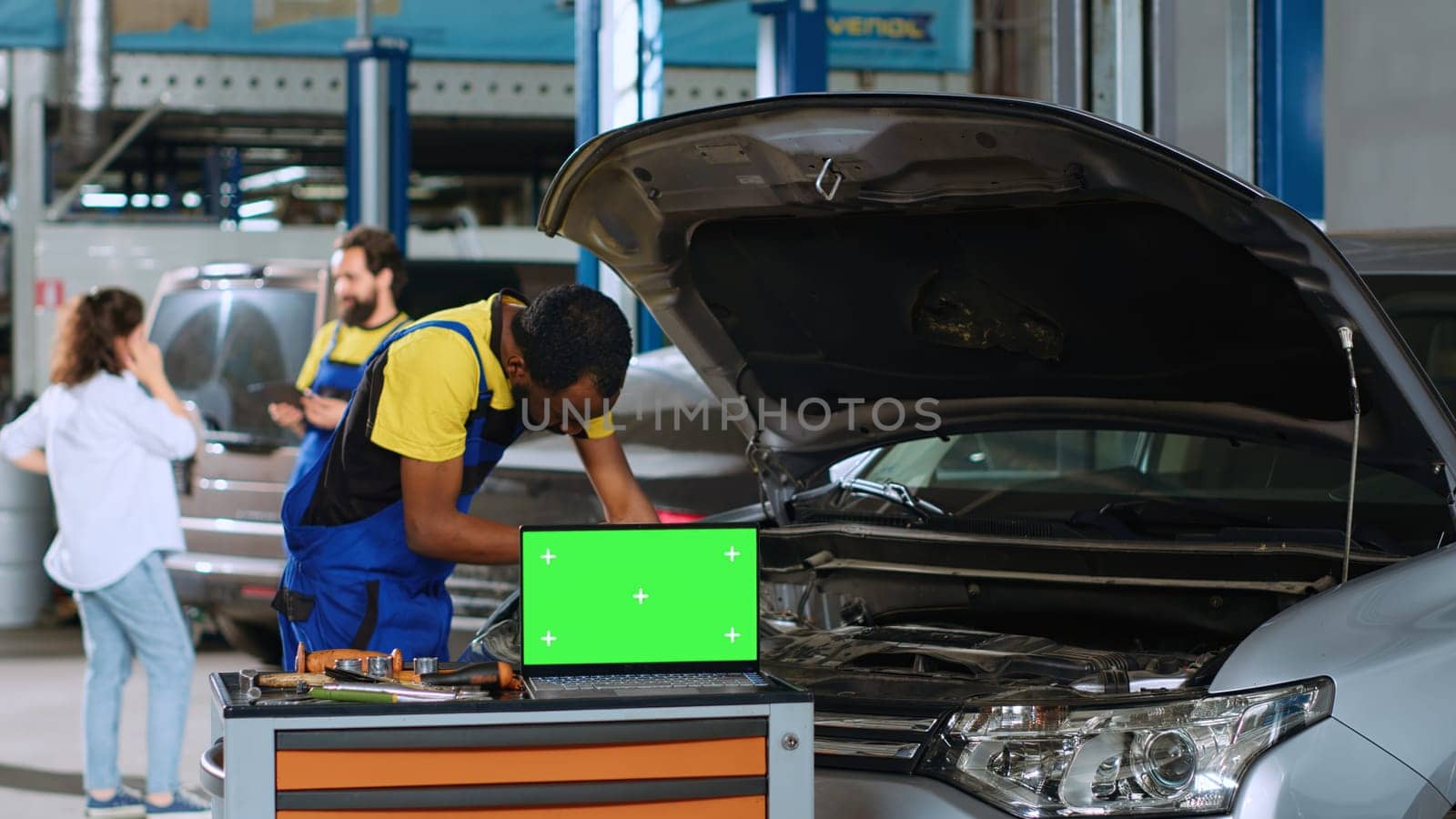 Engineer in car service uses torque wrench to tighten bolts inside vehicle with green screen laptop in front. Expert utilizes professional tools to mend automobile next to chroma key device