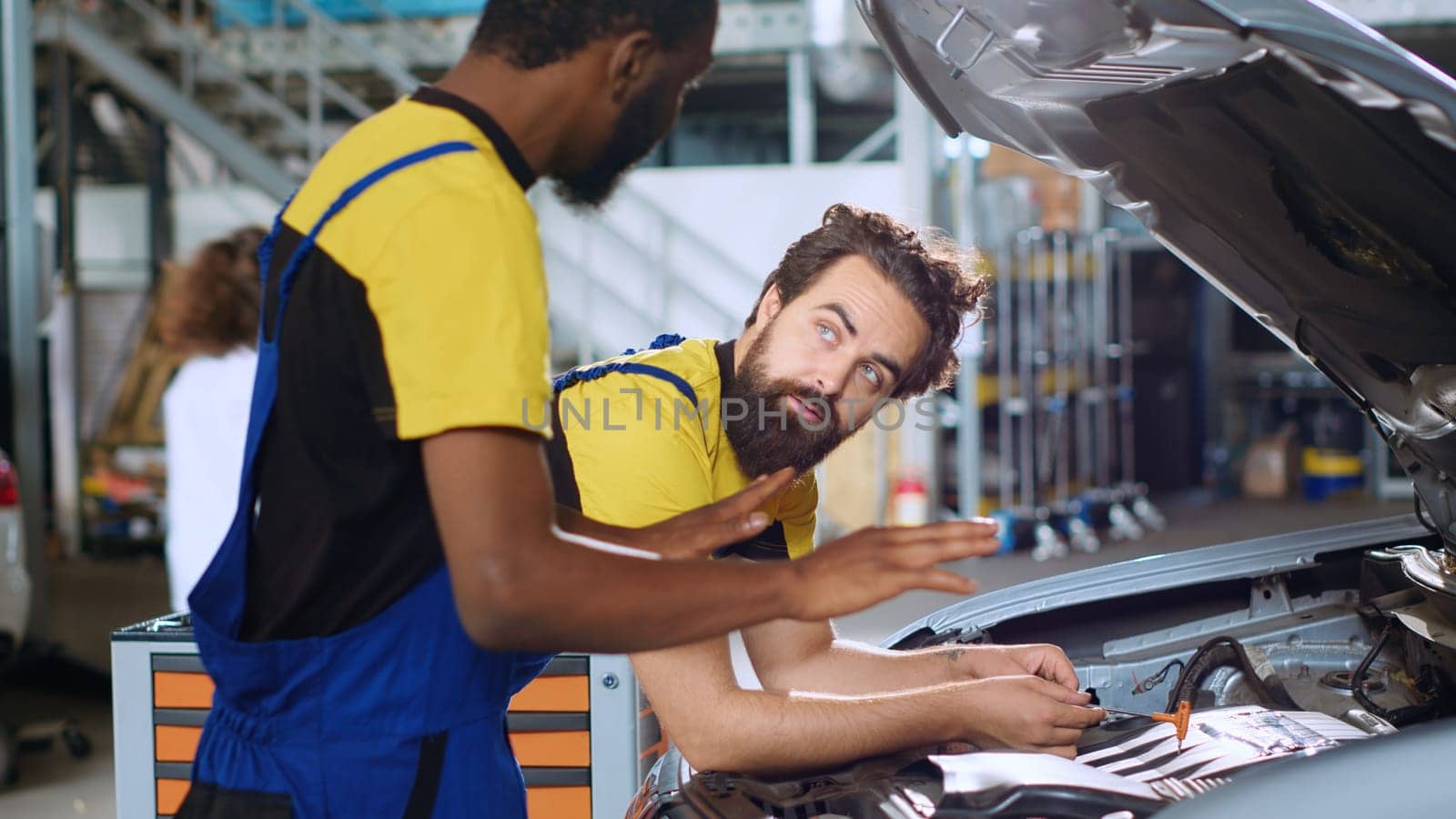 Qualified servicemen in auto repair shop working together on fixing car, discussing best options. Expert and colleague collaborating on servicing broken vehicle, checking for faulty components