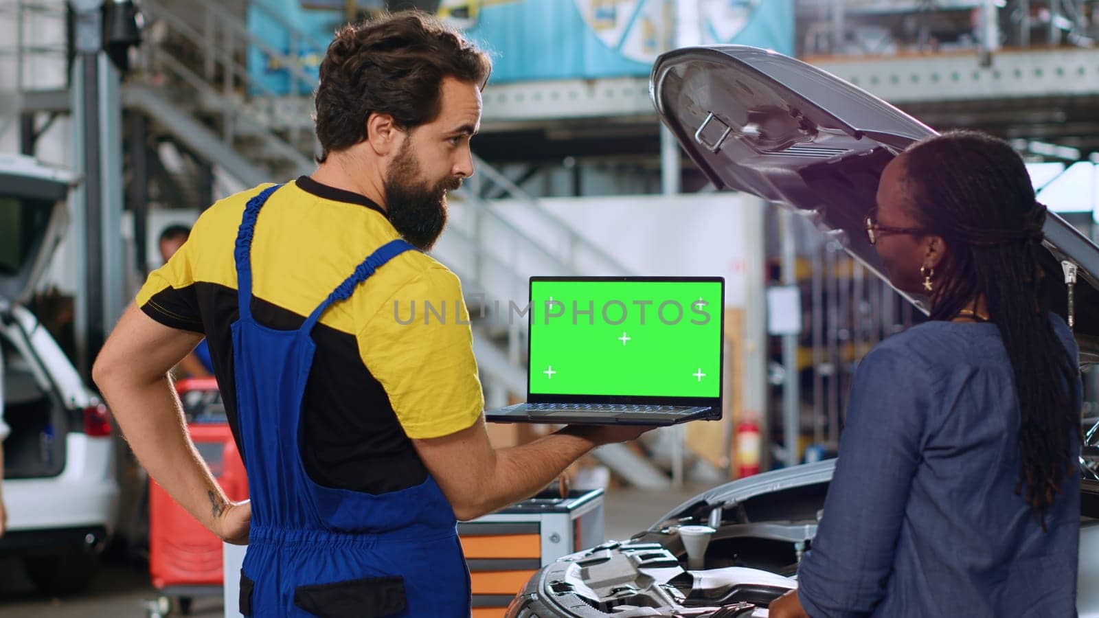 Trained serviceman using green screen laptop in car service to show customer parts needed for busted vehicle. Repair shop worker using chroma key device to search online for auto components