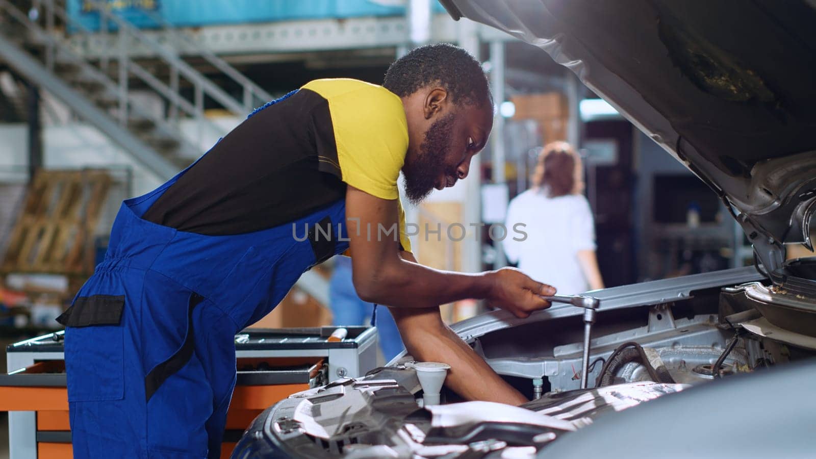 Experienced technician in car service uses torque wrench to tighten studs inside vehicle after fixing components inside. Specialist utilizes professional tools to refurbish automobile, handheld camera