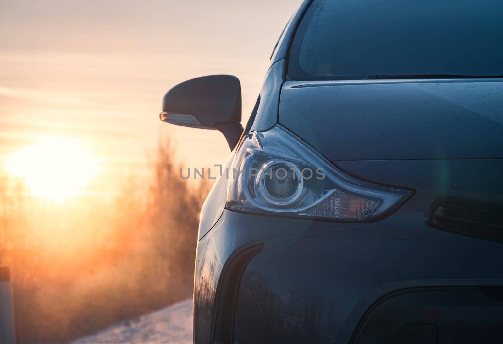 Dark gray car parked on snowy road at sunrise in winter countryside by Busker