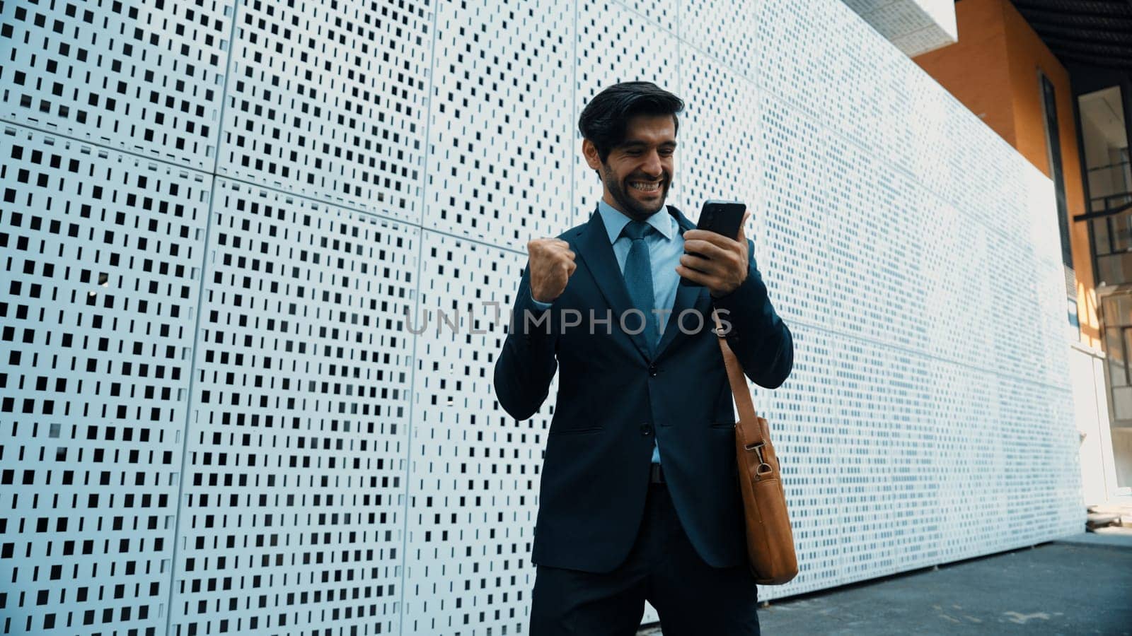 Happy smart business man celebrate for getting promotion or receive good news while walking at street. Skilled project manager or leader express feeling of overjoy at architectural building. Exultant