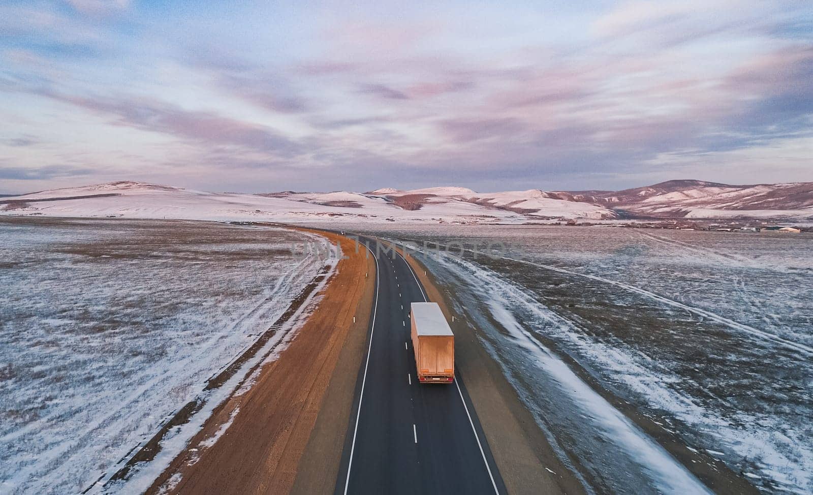 Lonely semi truck driving on snowy rural highway at dusk in winter landscape by Busker