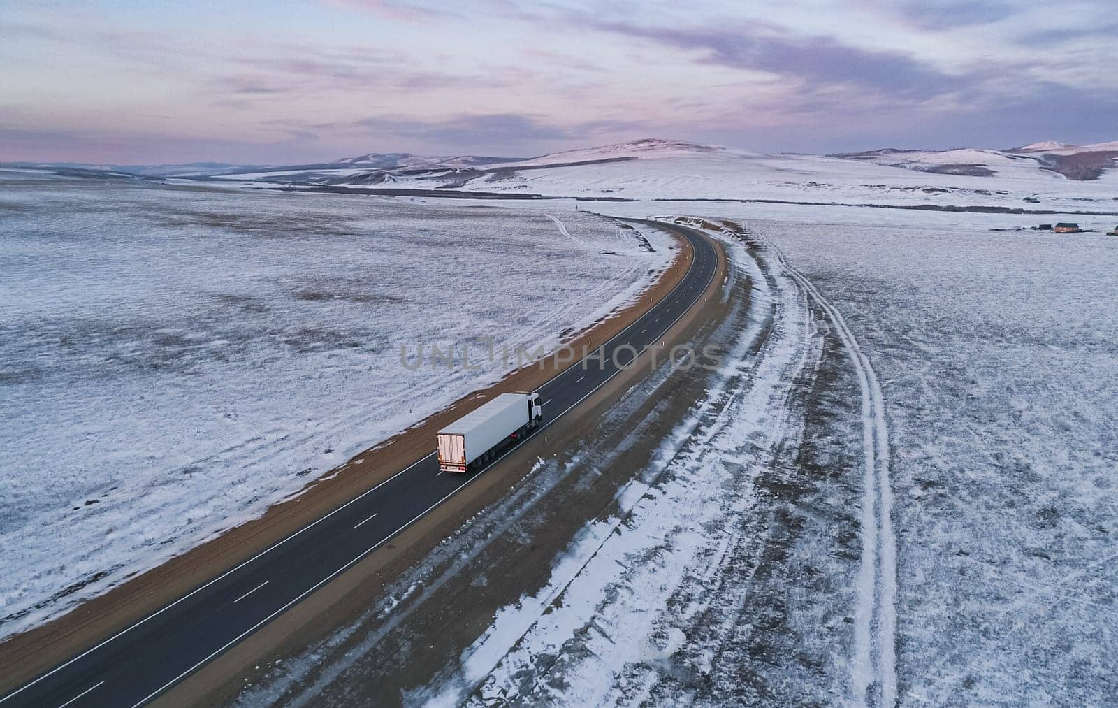 Lonely semi truck driving on snowy rural highway at dusk in winter landscape by Busker