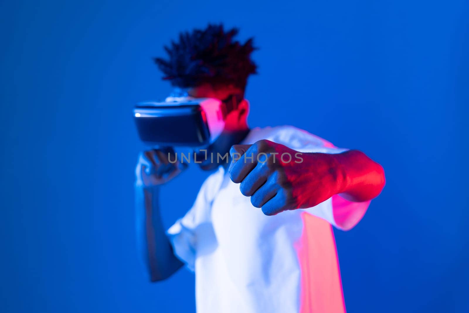 African American boxing gamer wearing VR playing boxer game punch camera posing isolated blue pink neon light wall connecting futuristic technology virtual reality metaverse fighting box. Contrivance.