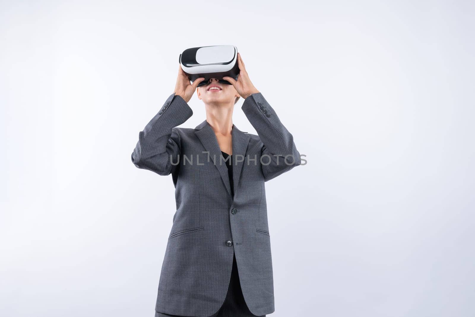 Skilled businesswoman looking at visual reality world by using VR glass while standing at background. Smart manager holding VR goggle to connect metaverse by using technology innovation. Contraption.