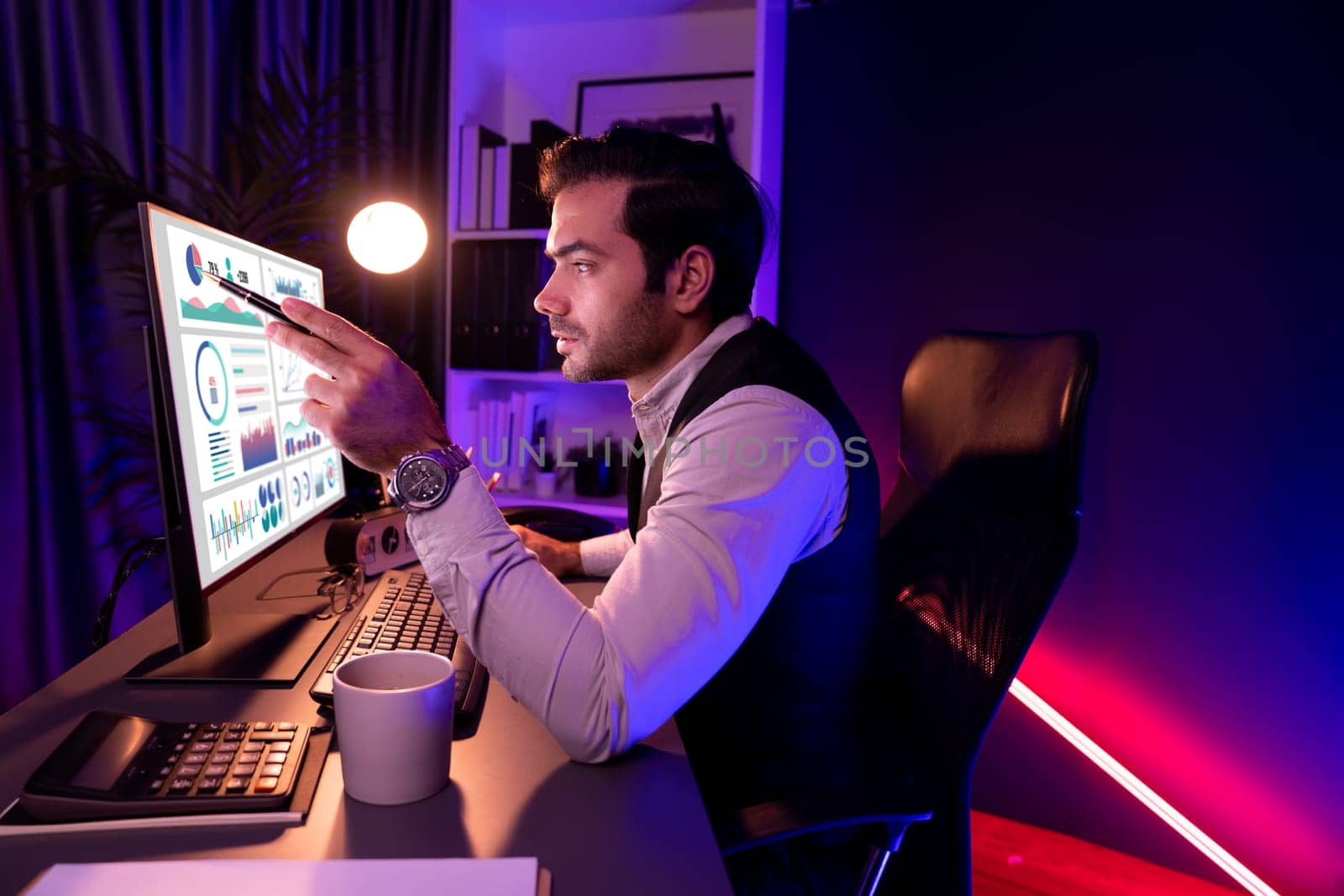 Smart businessman pointing with pen on desk to focusing research target market in service product database online channel on pc screen at purple neon dark light home office at night time. Surmise.