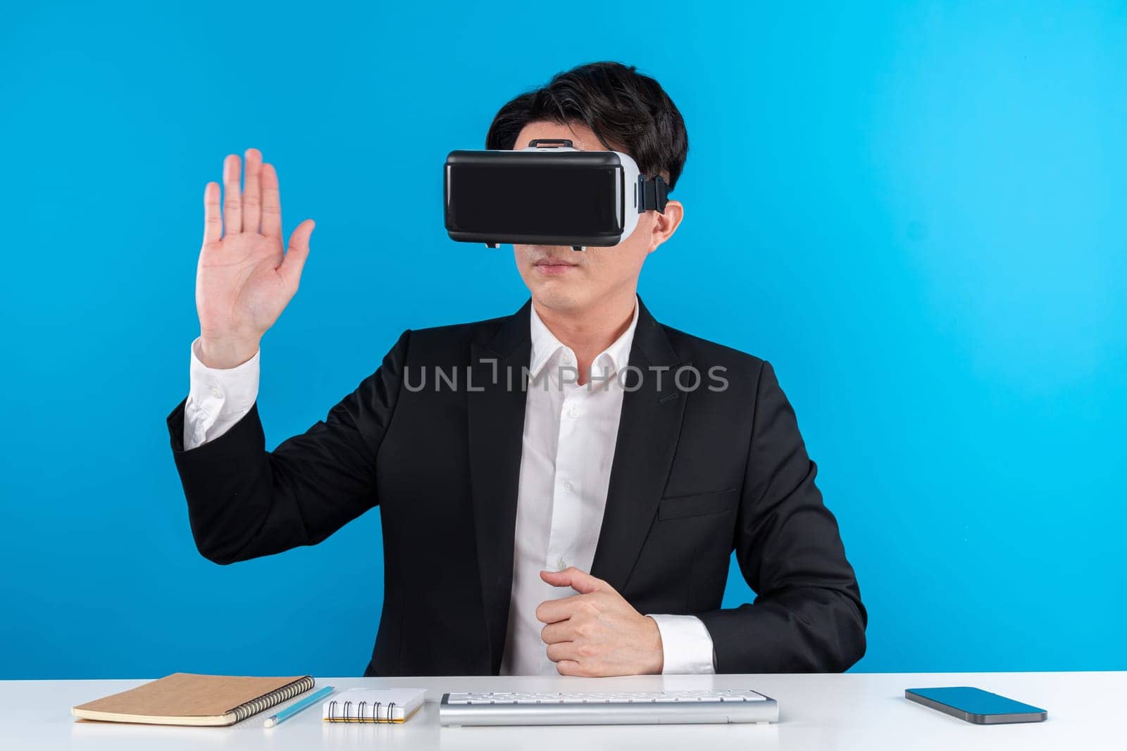 Asian businessman looking through VR connecting touchscreen hologram monitor in futuristic metaverse analyzing innovation technology business world virtual reality isolate blue copyspace. Contrivance.