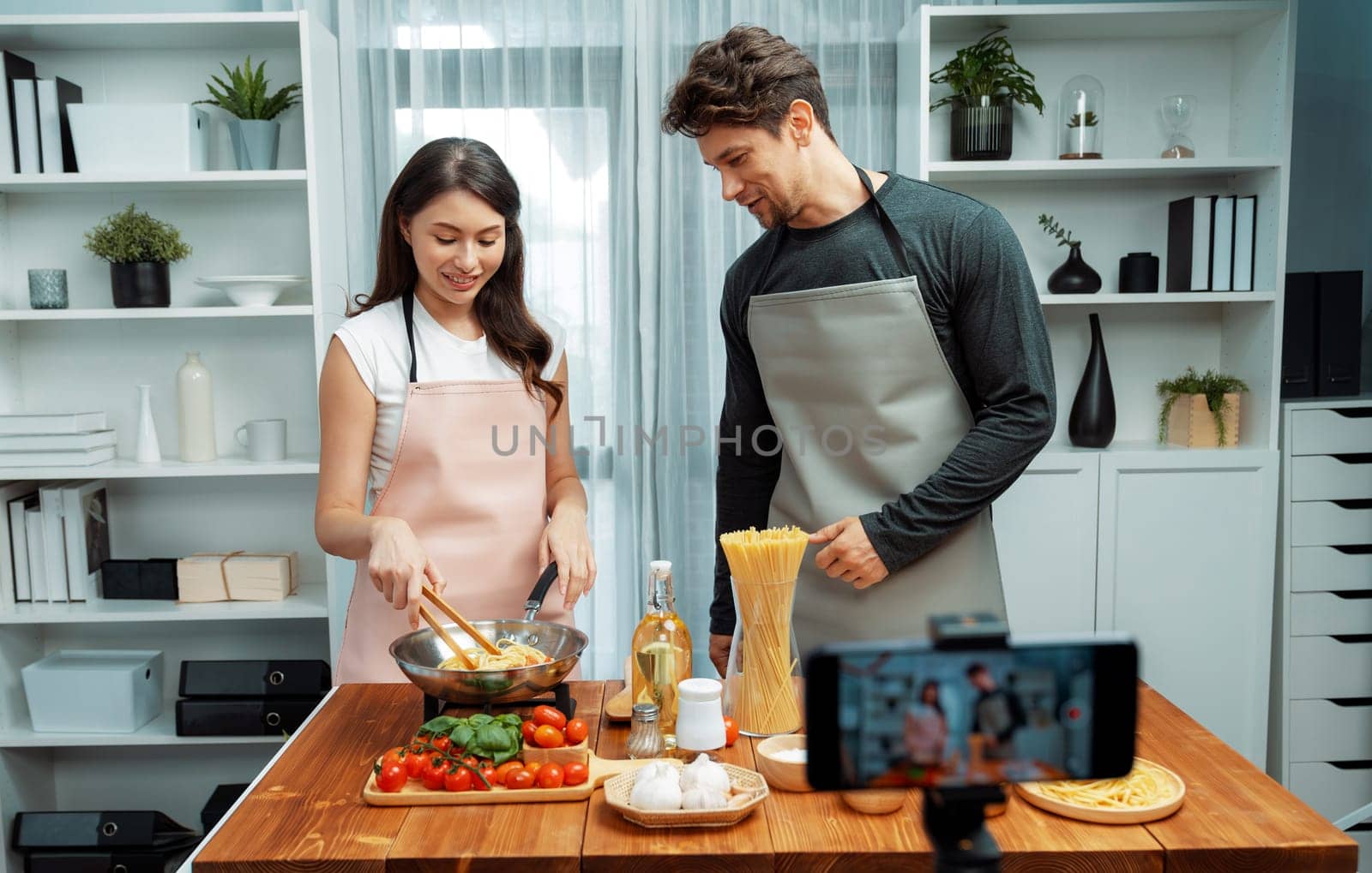 Couple chef influencers cooking special homemade of spaghetti mix ingredient taking to frying pan, putting seasoning and tasty sauce to make good flavor, recording on smartphone on chanel. Postulate.