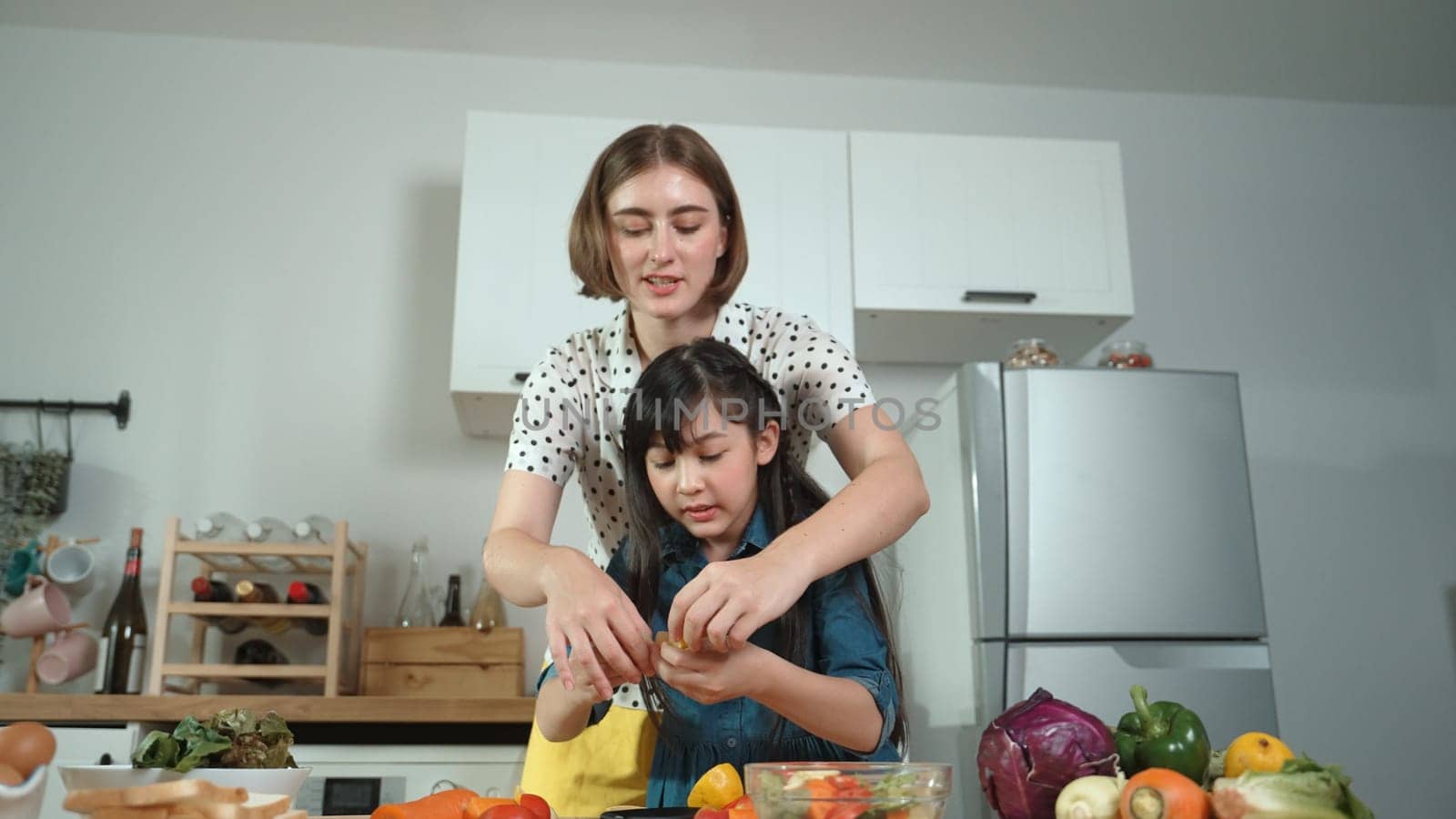 Smart caucasian mother and asian girl cooking together and chopping vegetable or preparing salad for dinner. Happy mom and daughter making healthy food with fresh food. Healthy food concept. Pedagogy.