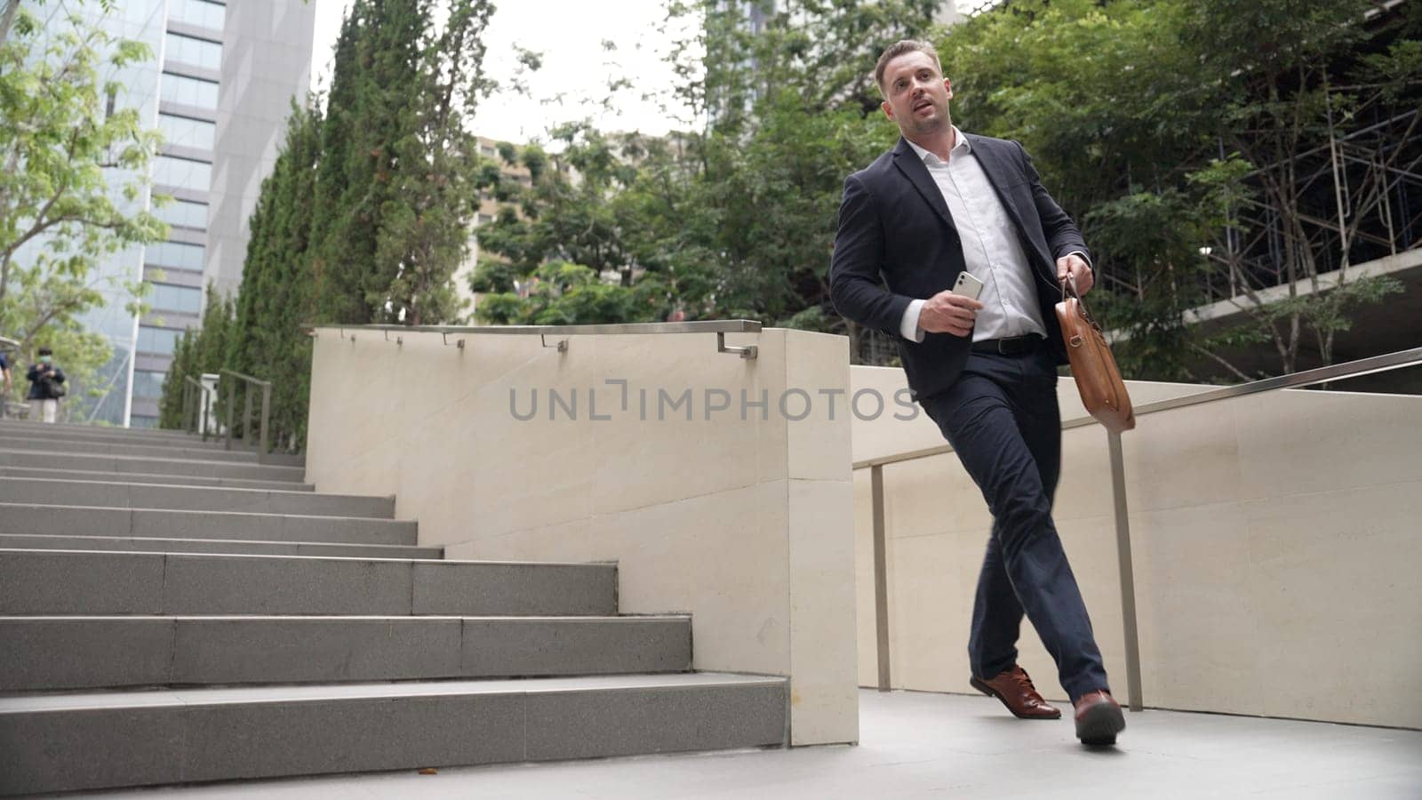 Worried smart business man running up stairs with hurry at green eco city. Anxious project manager rushing for not being late in important meeting while going to workplace at park. Lifestyle. Urbane.