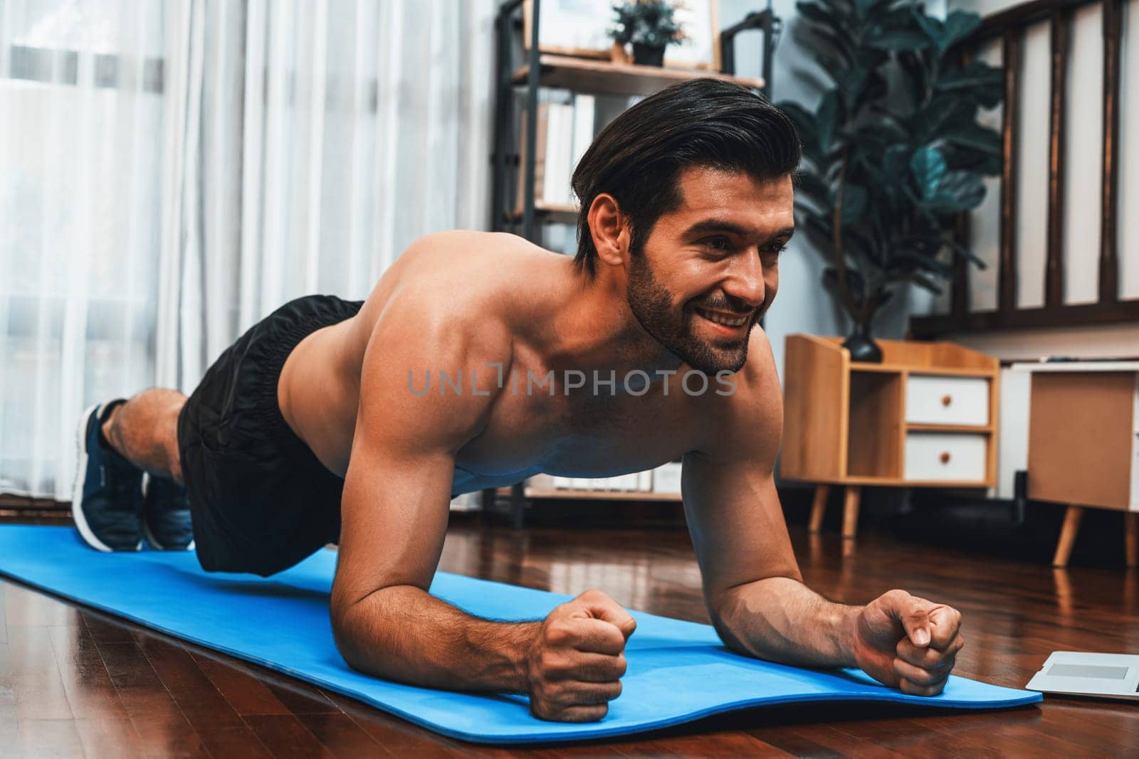 Athletic and sporty man doing plank on fitness mat at gaiety home. by biancoblue