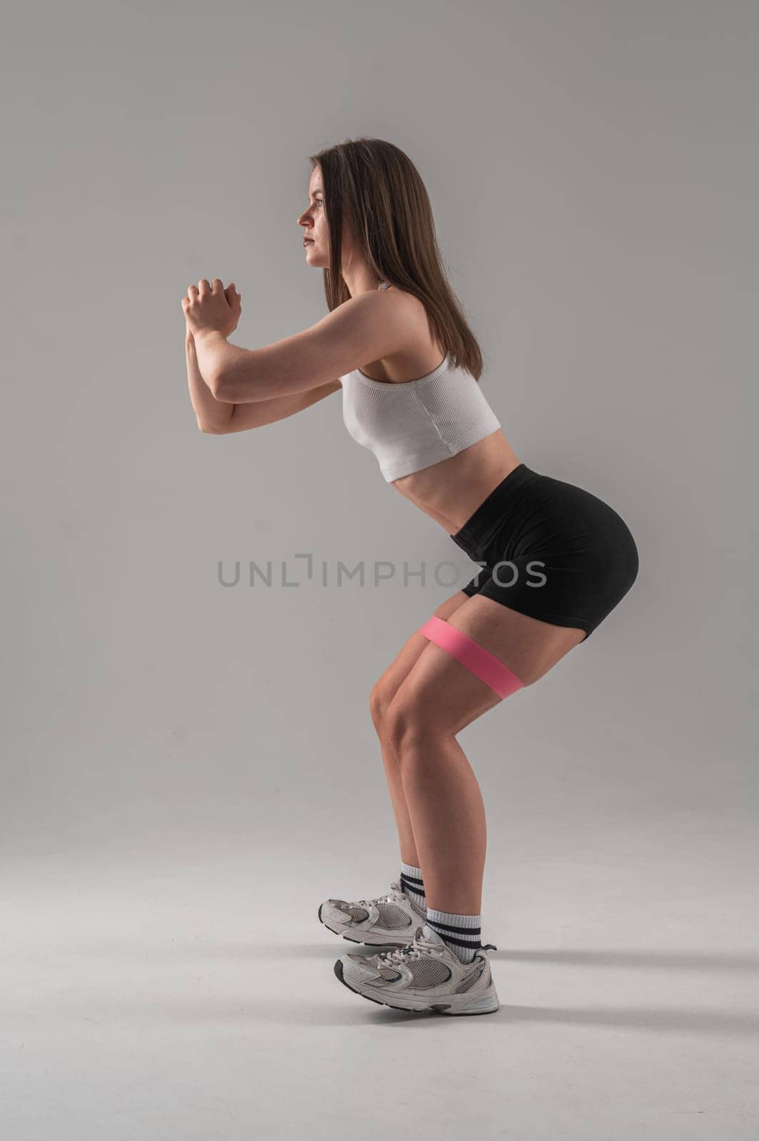 Caucasian woman doing squats with fitness band on white background. Vertical photo