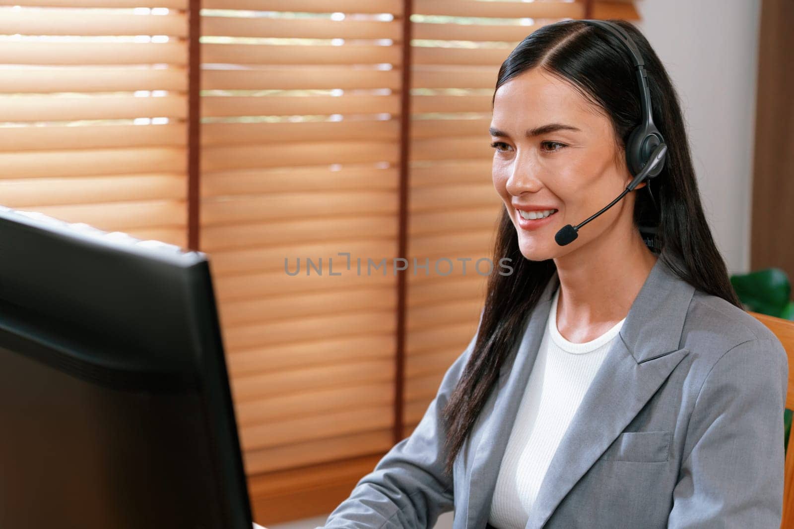 Female call center operator or customer service helpdesk staff working on workspace while talking on the headset to provide assistance for customer. Professional modern business service. Blithe