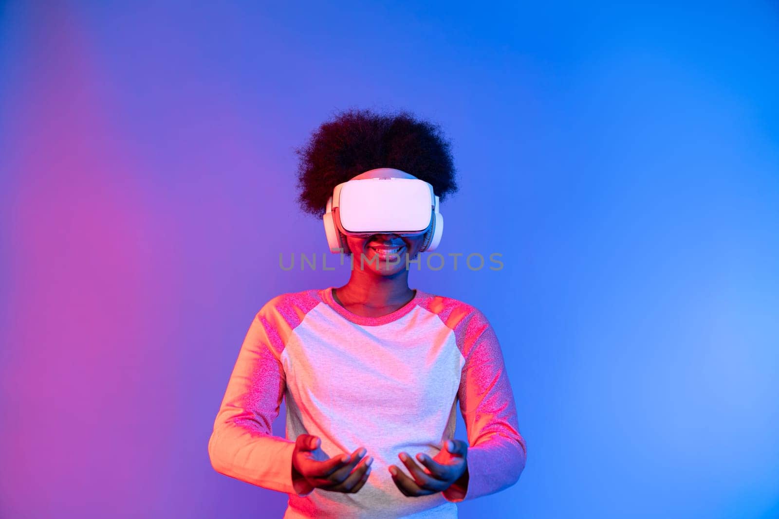 Young African wearing VR glasses through metaverse holding data learning application on blue pink neon lighting gradient technology digital innovation 3D studying hologram graphic assist. Contrivance.