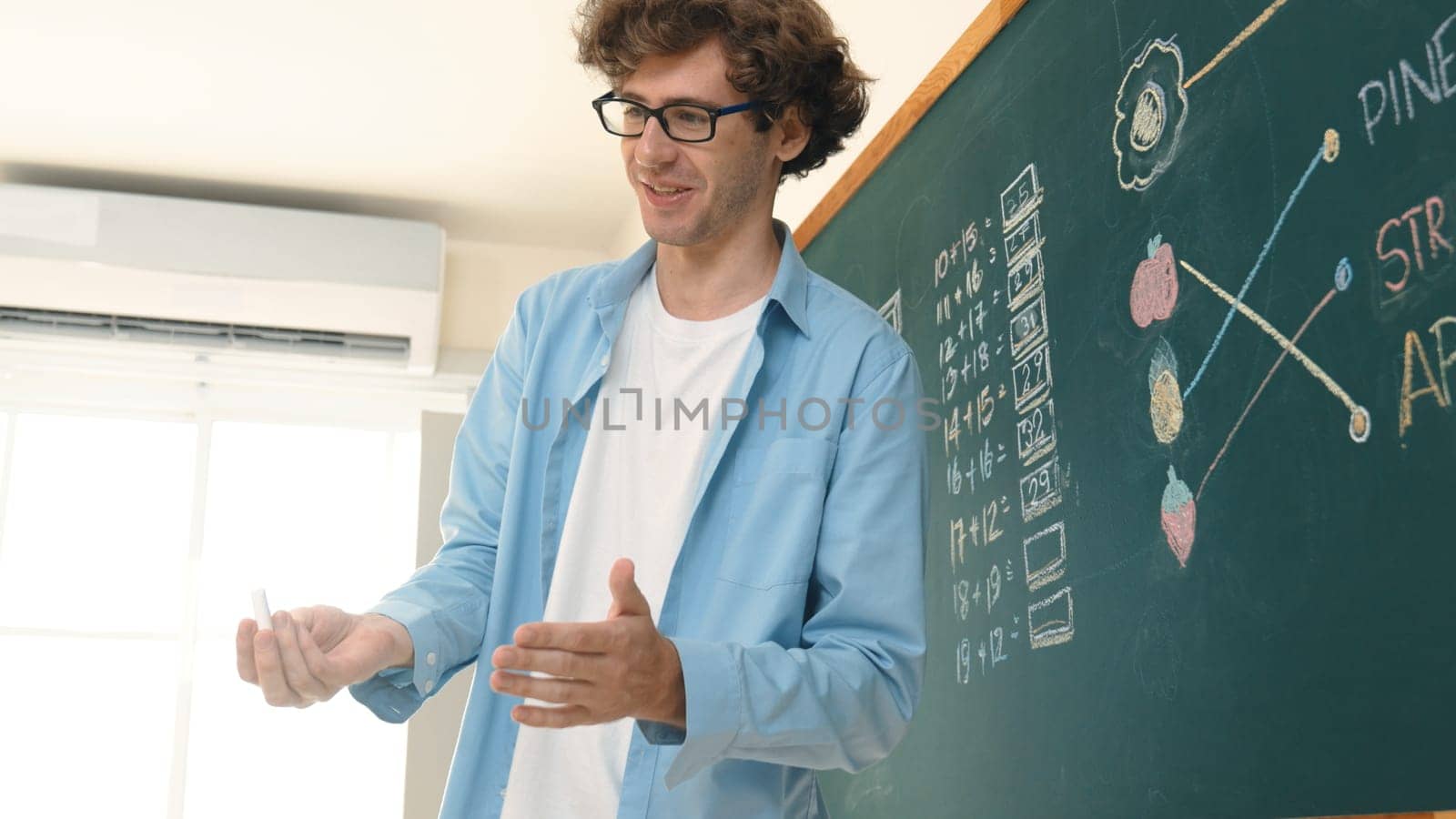 Caucasian teacher talking and explain about math theory at classroom while looking at student. Smart skilled instructor teaching and pointing at blackboard while standing in front of board. Pedagogy.