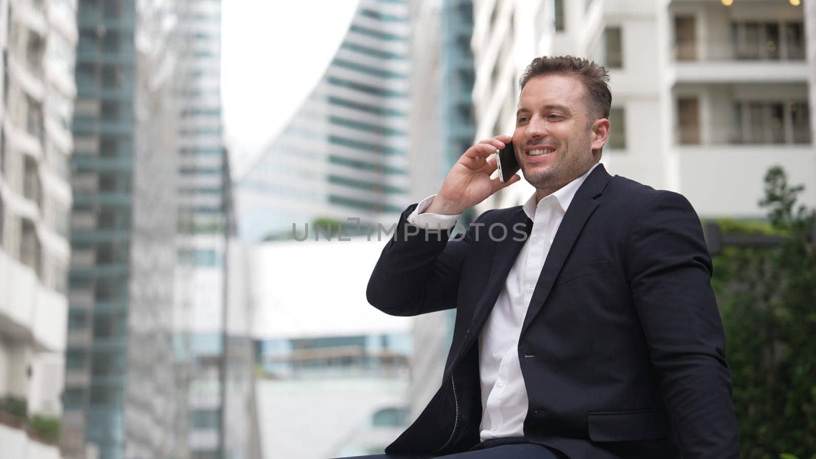 Caucasian businessman sitting at bench while talking to manager by using phone about planning strategy. Professional executive manager calling marketing team and sharing creative idea at city.Urbane.