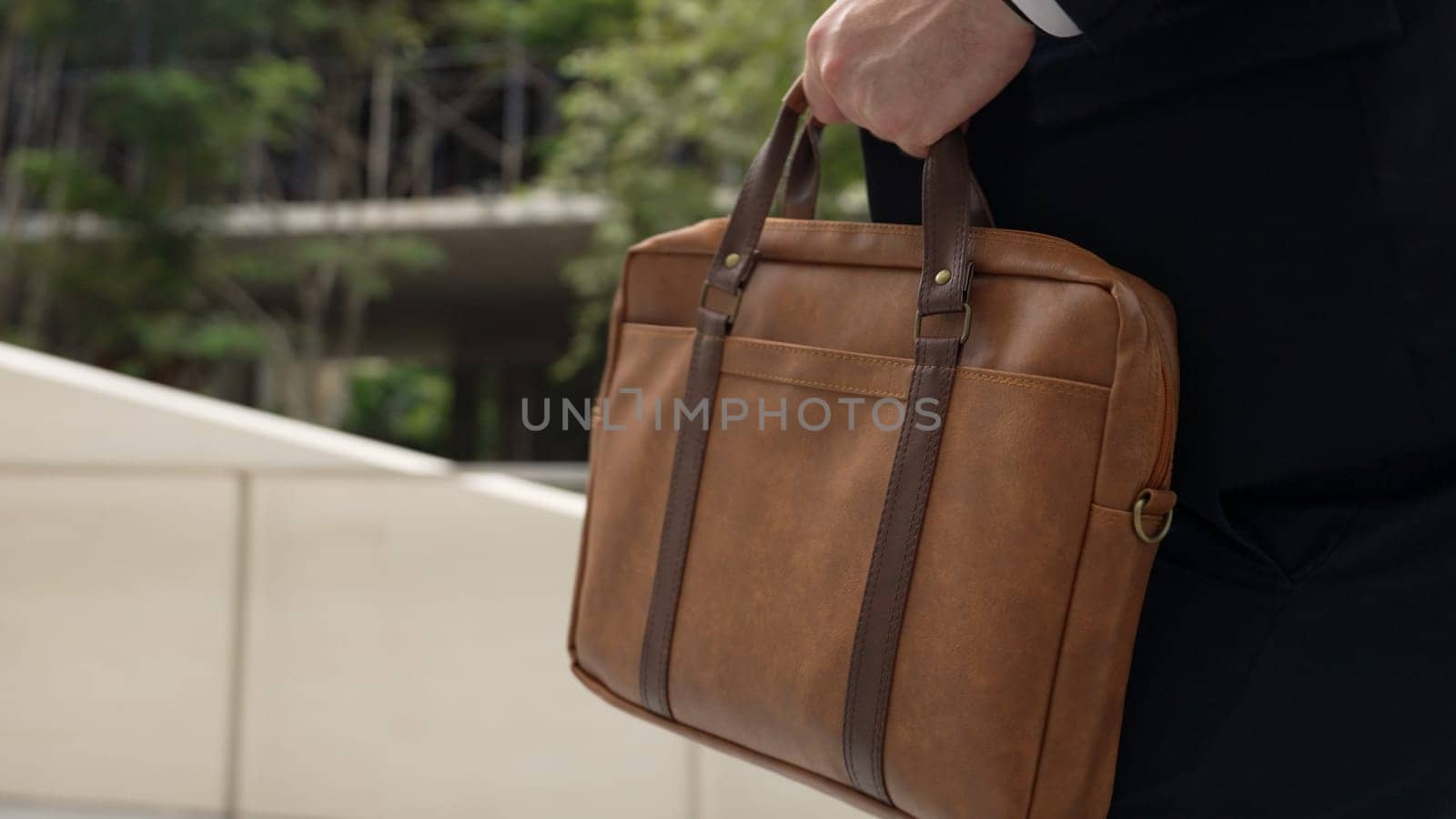 Close up of suitcase was held by profession businessman while project manager walking up stairs or step to new position at green eco city. Happy project manager using travel bag. Focus on bag. Urbane.