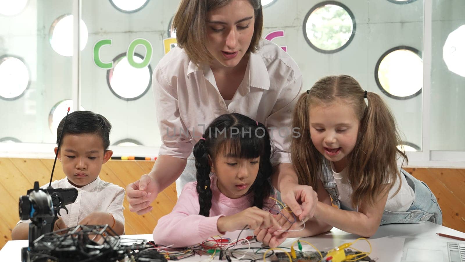 Teacher looking at children while diverse student looking at screen. Children excited in presentation while drawing or writing art books at table with toys and color pencil placed on table. Erudition.