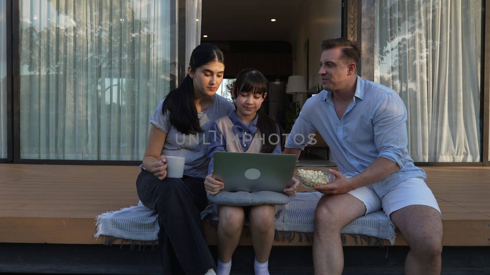 Father, mother and daughter focus laptop at terrace with garden view outside house. Parent use outdoor activity to communicate young generation about environment care cross generation gap. Divergence.