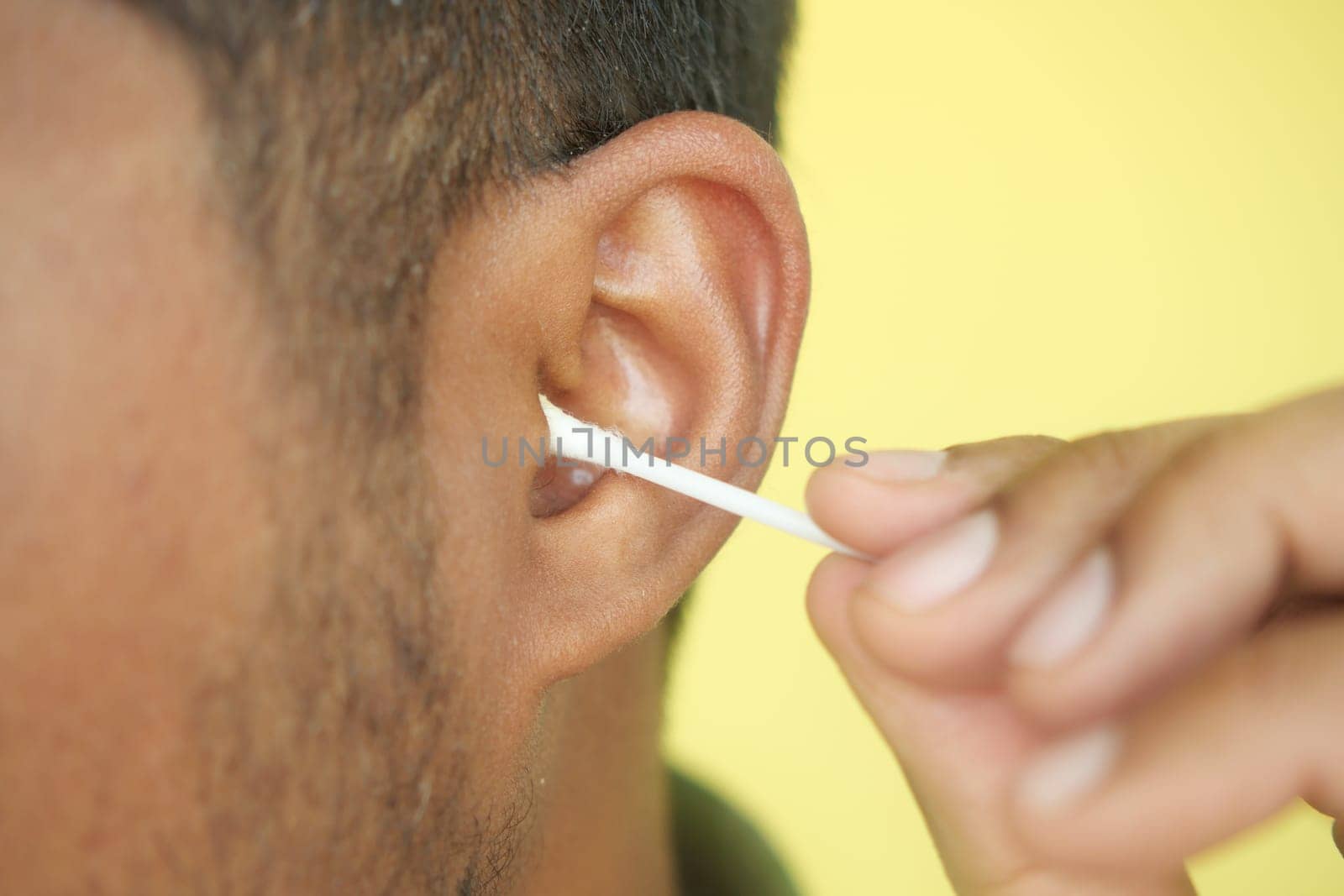 Closeup of young man using ear cotton bar.