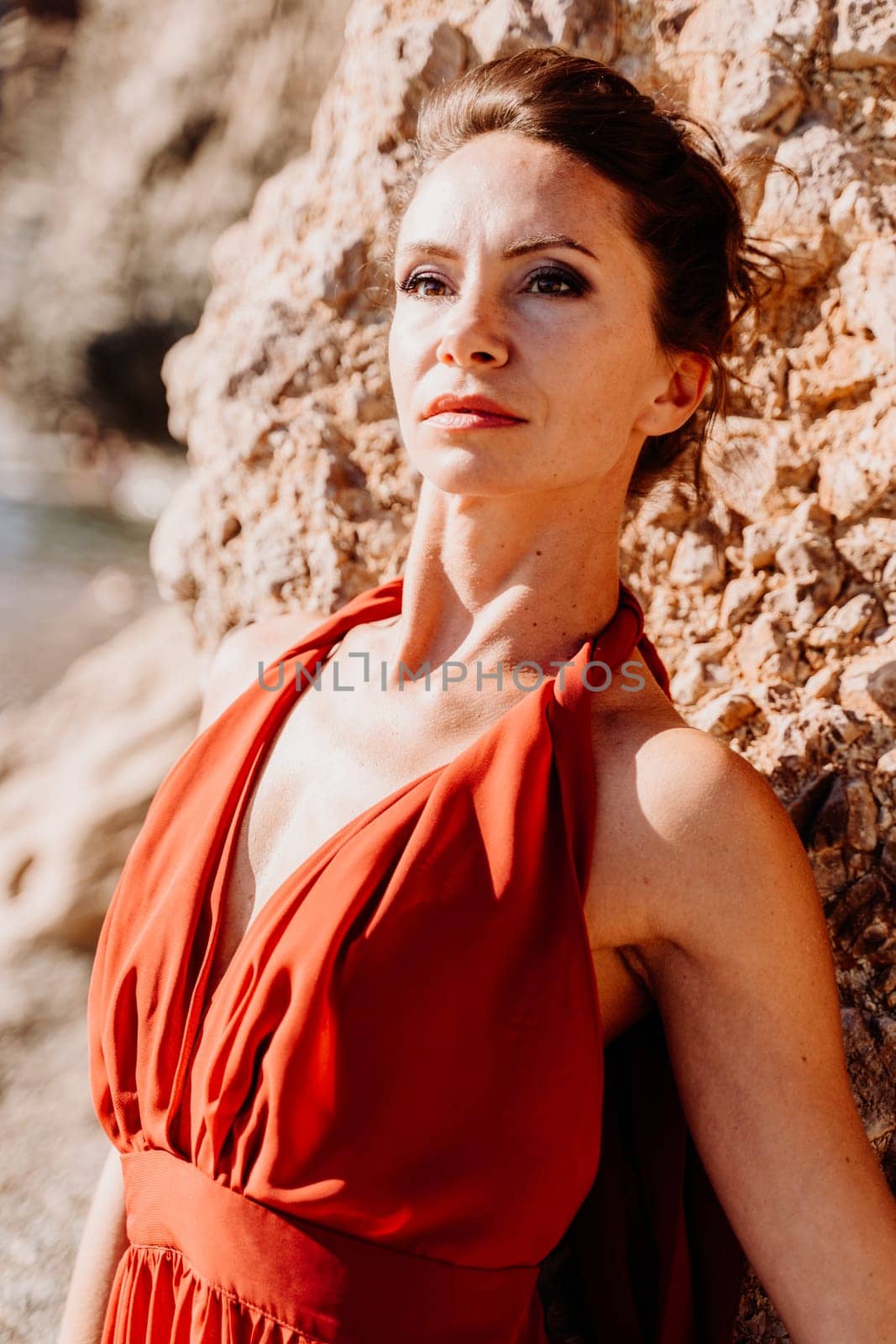 Woman red dress sea. Woman in a long red dress posing on a beach with rocks on sunny day. Girl on the nature on blue sky background. by Matiunina
