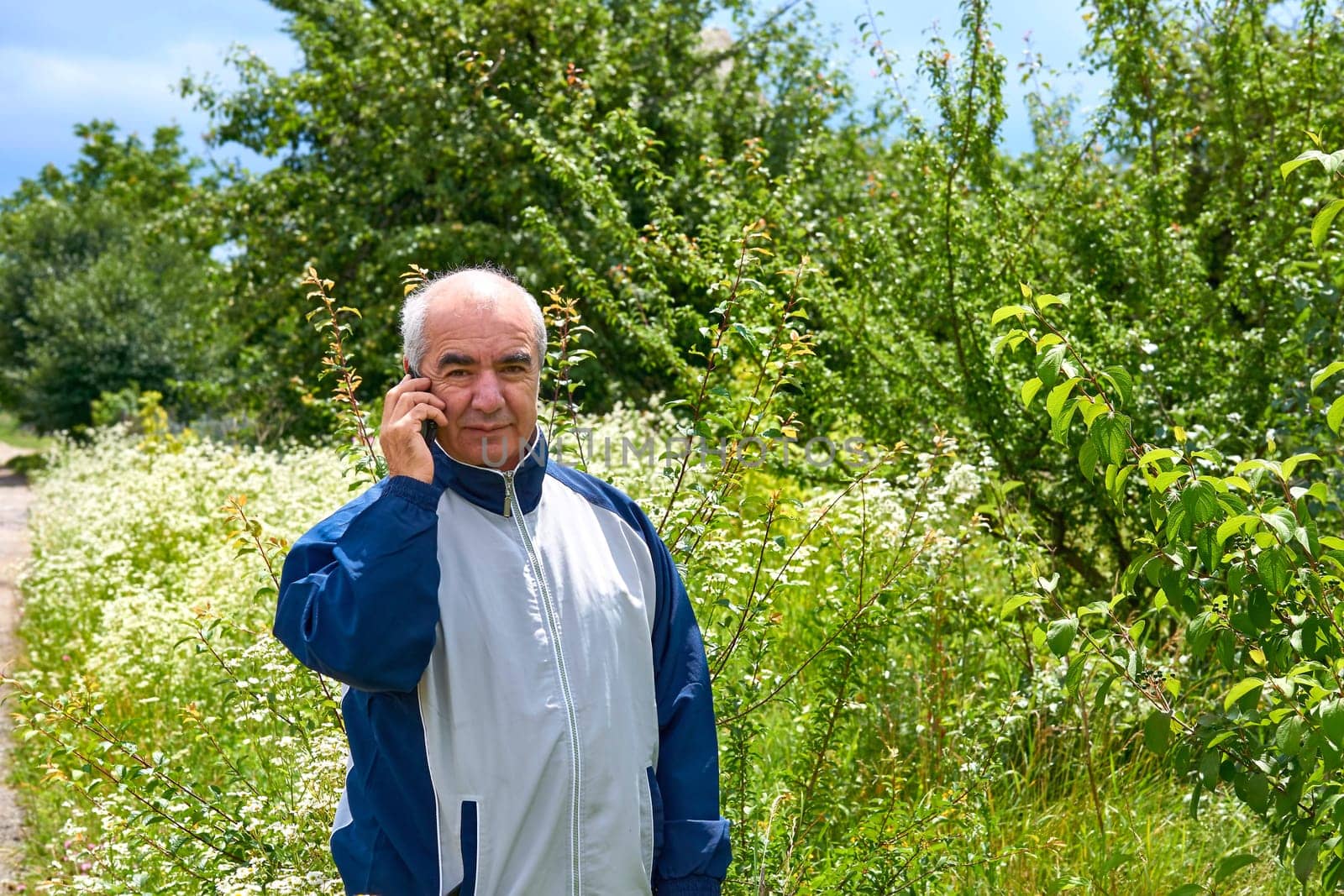 Elderly retired man walking talking on the phone in a august september garden by jovani68